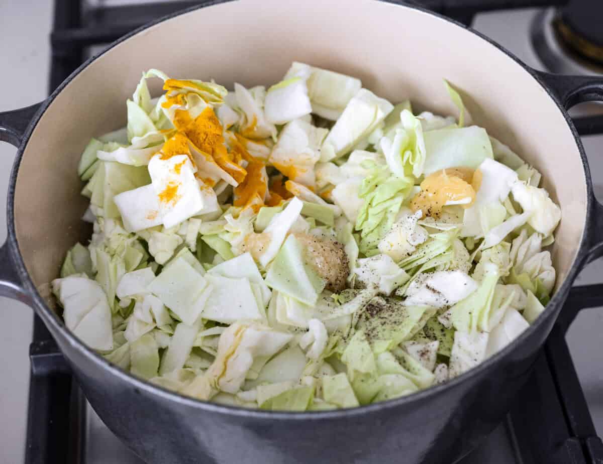 This Detox Cabbage Soup is the perfect way to kick off your New Year's resolutions! After indulging over the holidays, this soup will give you the kick-start you need to feel better. It's loaded with fresh veggies and essential vitamins and is super budget-friendly. Overhead shot of the cabbage, turmeric, ginger, garlic, salt and pepper being added to the pot.