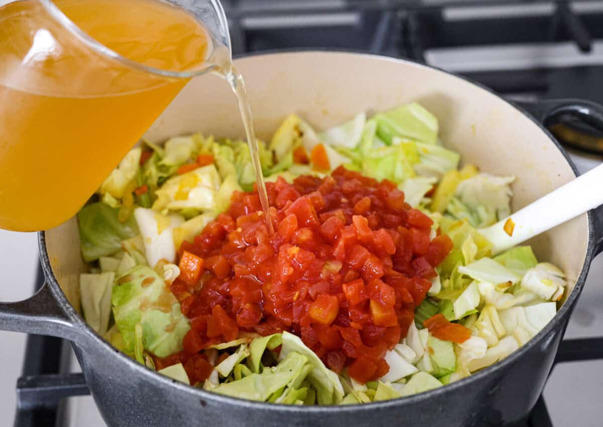 This Detox Cabbage Soup is the perfect way to kick off your New Year's resolutions! After indulging over the holidays, this soup will give you the kick-start you need to feel better. It's loaded with fresh veggies and essential vitamins and is super budget-friendly. Angle shot of the vegetables, seasonings and cabbage with the tomatoes and vegetable broth on top.