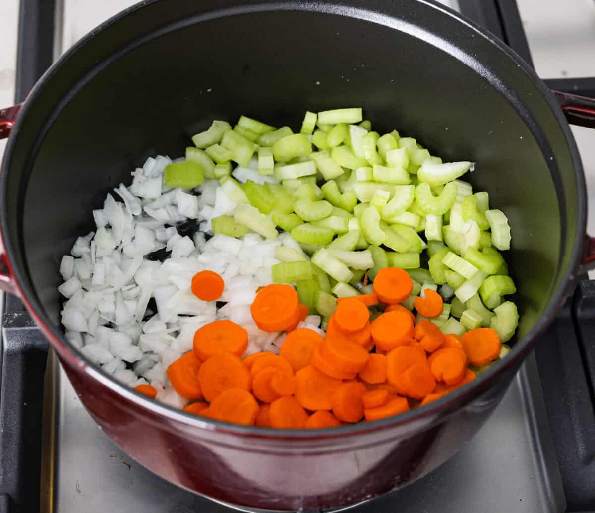 Tuscan white bean soup is like a warm hug in a bowl. Hearty beans and tender vegetables come together to give you a boost of nutrients. This soup is light and fresh tasting, with bright, zesty flavors! Overhead shot of celery, onions and carrots in a pot with olive oil.