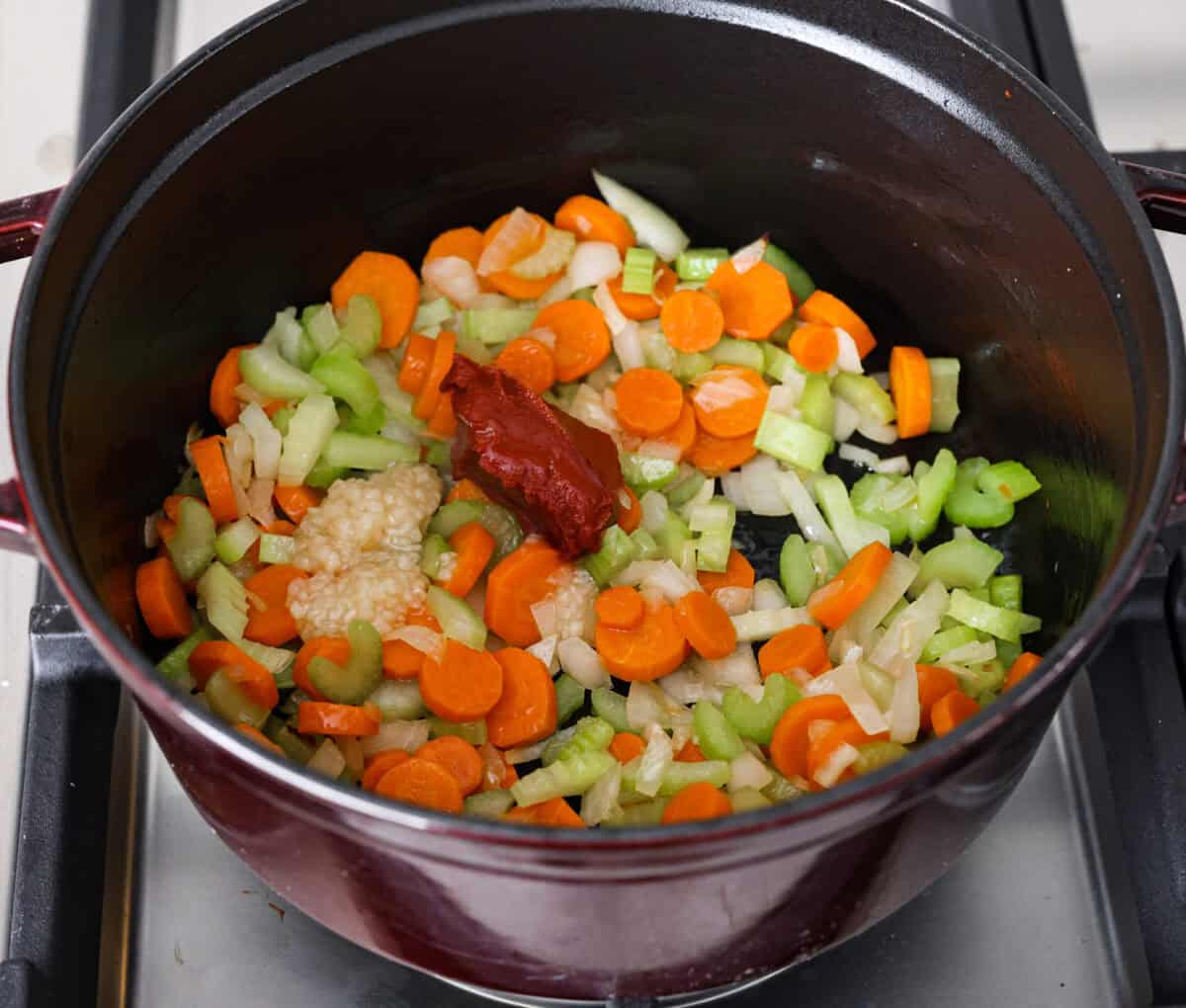 Tuscan white bean soup is like a warm hug in a bowl. Hearty beans and tender vegetables come together to give you a boost of nutrients. This soup is light and fresh tasting, with bright, zesty flavors! Overhead shot of partially cooked vegetables with garlic and tomato past added.