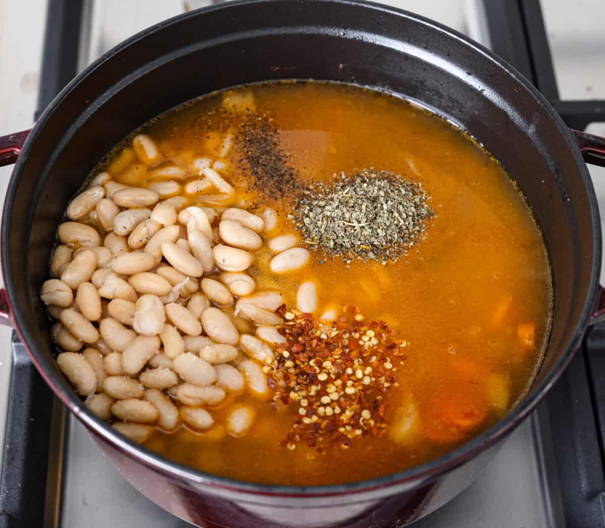 Tuscan white bean soup is like a warm hug in a bowl. Hearty beans and tender vegetables come together to give you a boost of nutrients. This soup is light and fresh tasting, with bright, zesty flavors! Overhead shot of beans, broth, seasonings, and vinegar added to. the vegetables.