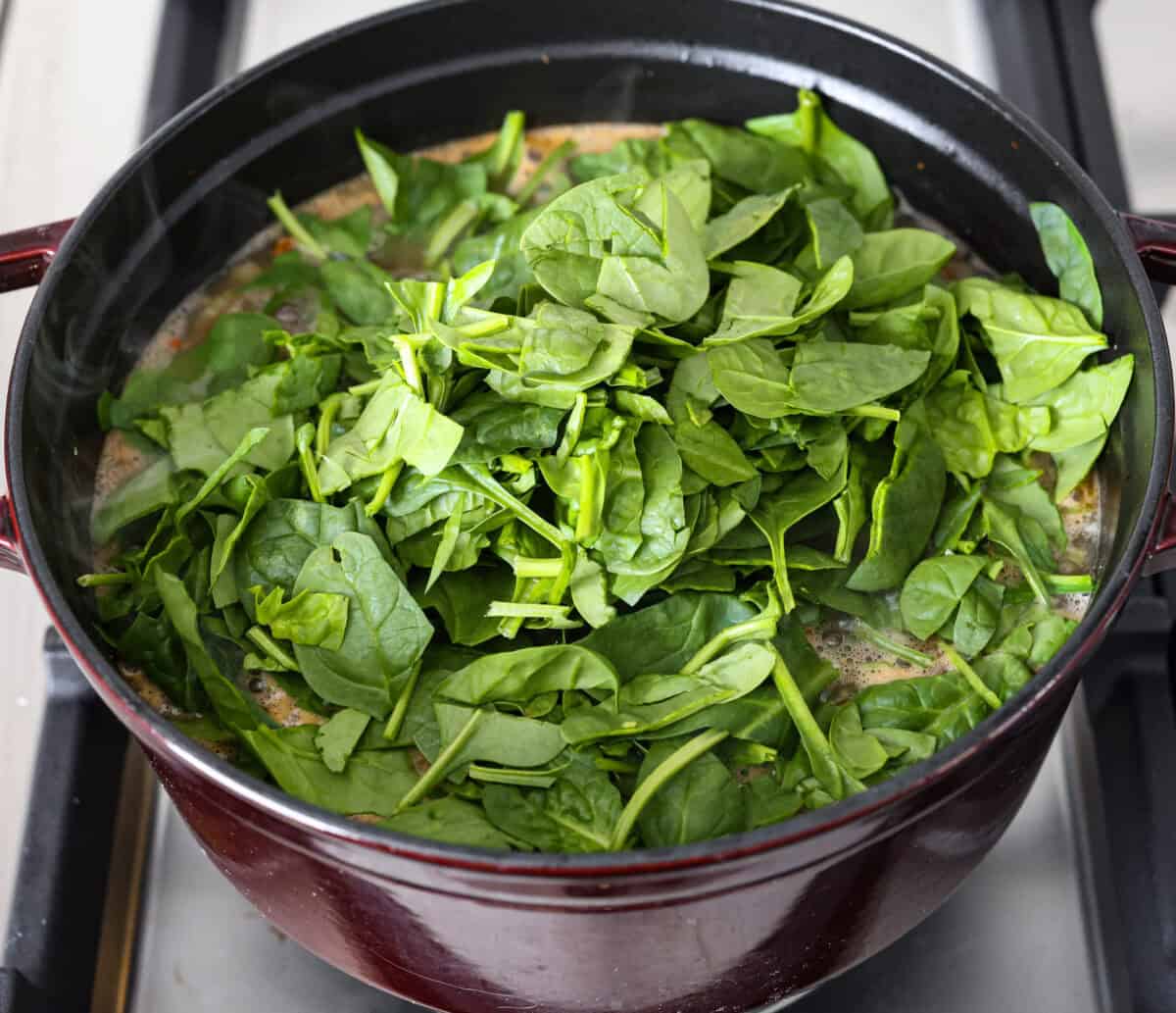 Tuscan white bean soup is like a warm hug in a bowl. Hearty beans and tender vegetables come together to give you a boost of nutrients. This soup is light and fresh tasting, with bright, zesty flavors! Overhead shot of spinach on top of the rest of the soup ingredients.