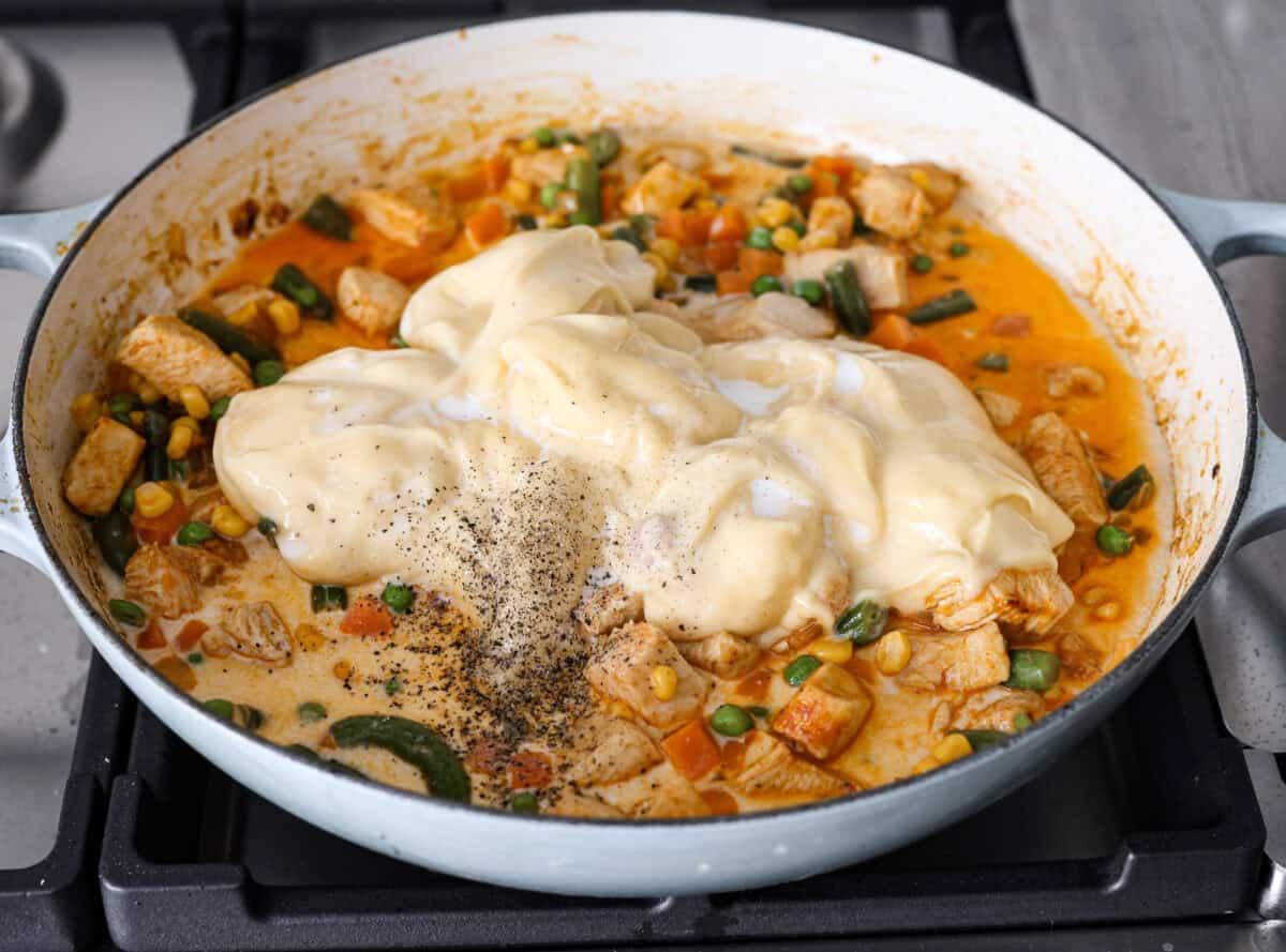 Chicken Pot Pie Pasta is a quick and easy twist on the classic comfort food. This one-pan recipe includes all the creamy, hearty flavors of a traditional chicken pot pie but swaps the pie crust for tender noodles. Itโs a simple, fuss-free meal ready in just 30 minutes! Angle shot of the veggies added in with the chicken and onion mixture with milk, soup and salt and pepper over the top.