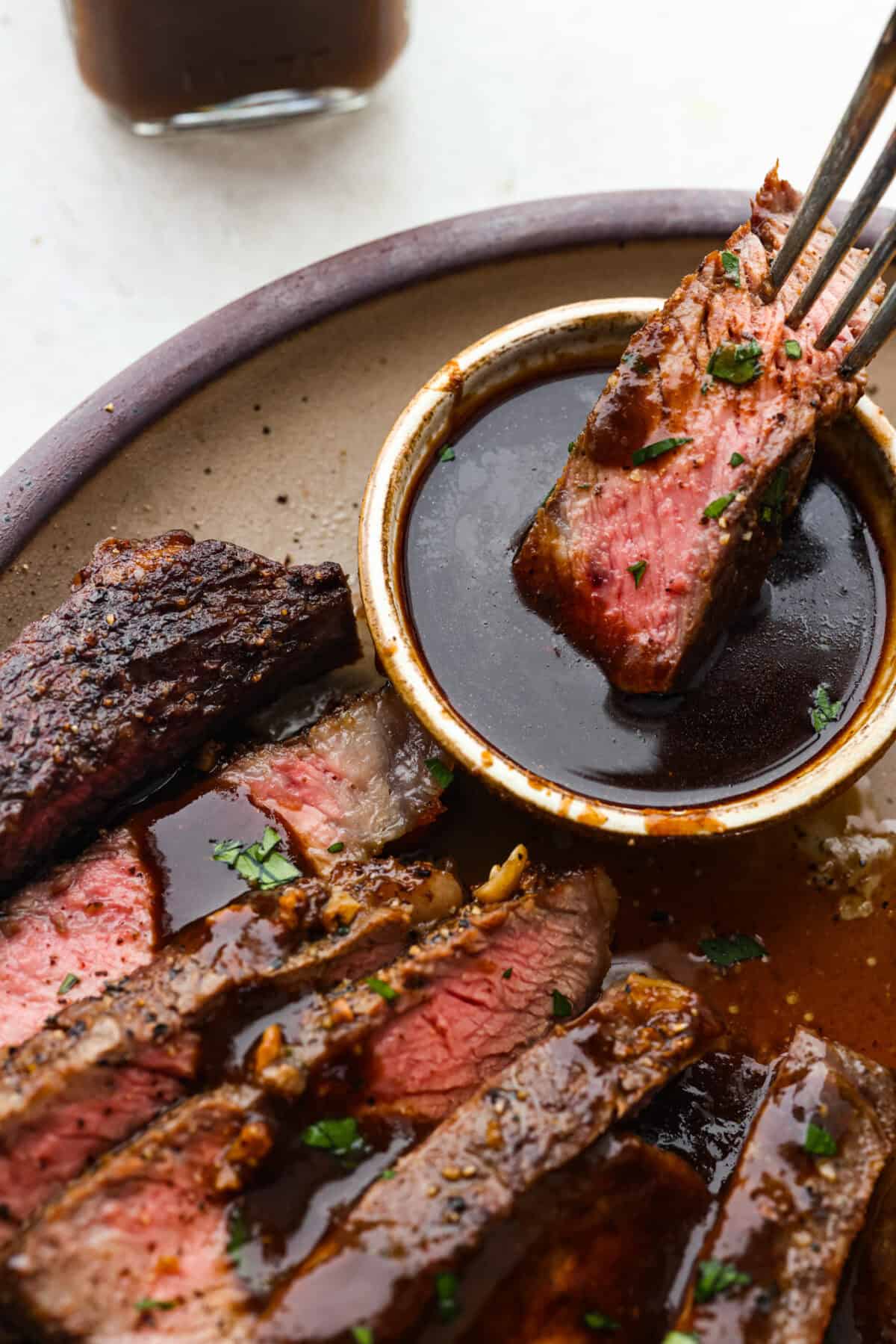 This A-1 copycat homemade steak sauce recipe is slightly sweet with a delicious tang from the vinegar. It's perfect for drizzling over your favorite cut of tender, juicy meat. Angle shot of someone dipping a piece of steak into the homemade steak sauce.