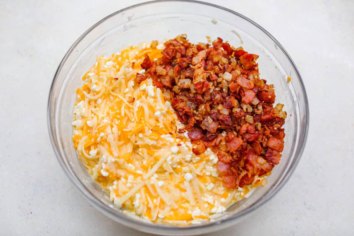 Kickstart your day with this hearty Amish Breakfast Casserole! It's loaded with crispy bacon, tender hash browns, and gooey melted cheese. This dish is a crowd-pleaser thatโs perfect for family breakfasts and holiday mornings! Overhead shot of the cheese and potato mixture with bacon and onion mixture in a bowl.