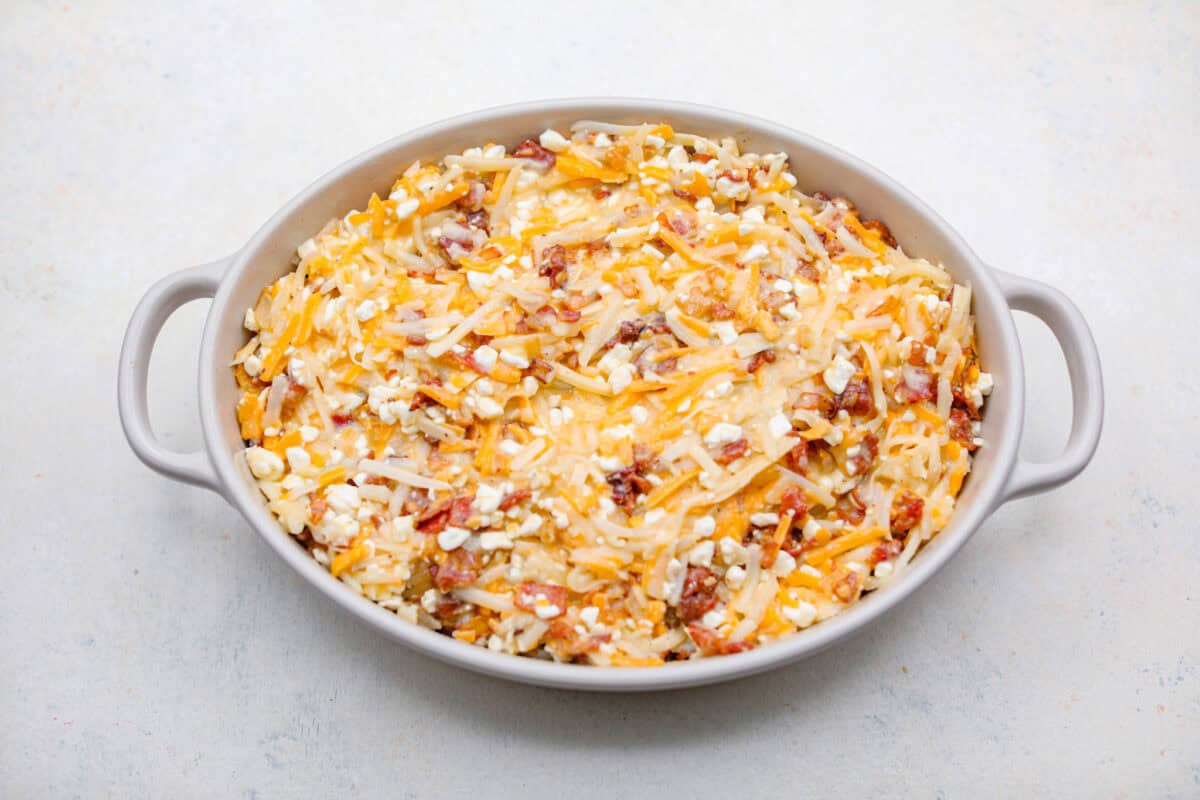 Kickstart your day with this hearty Amish Breakfast Casserole! It's loaded with crispy bacon, tender hash browns, and gooey melted cheese. This dish is a crowd-pleaser thatโs perfect for family breakfasts and holiday mornings! Overhead shot of amish breakfast casserole ingredients in a baking dish ready to be cooked.