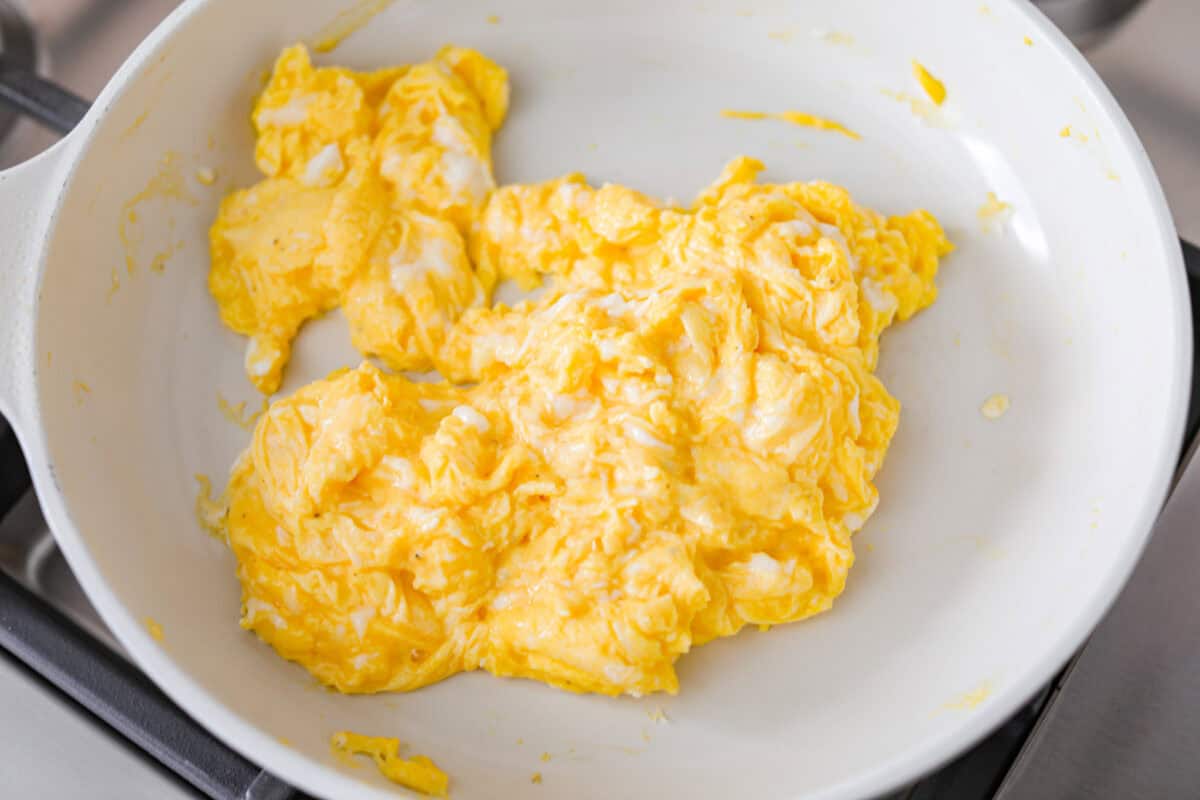 This Breakfast Stromboli is the best morning treat! It's packed with fluffy eggs, savory sausage, crispy bacon, and melty cheese, all wrapped in golden pizza dough. Perfect for holiday brunches or everyday family breakfasts! Overhead shot of scrambled eggs in a skillet.