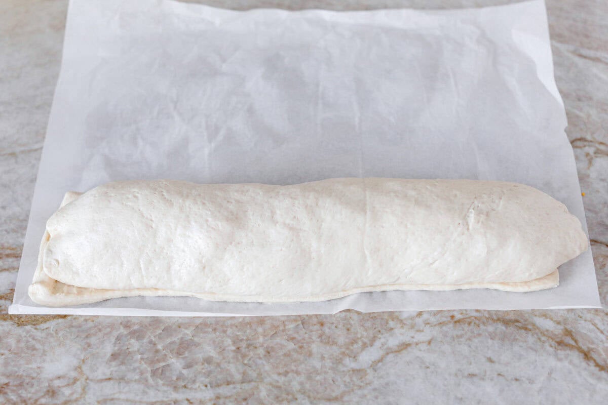 This Breakfast Stromboli is the best morning treat! It's packed with fluffy eggs, savory sausage, crispy bacon, and melty cheese, all wrapped in golden pizza dough. Perfect for holiday brunches or everyday family breakfasts! Angle shot of the Stromboli wrapped and rolled over with the seem side down.