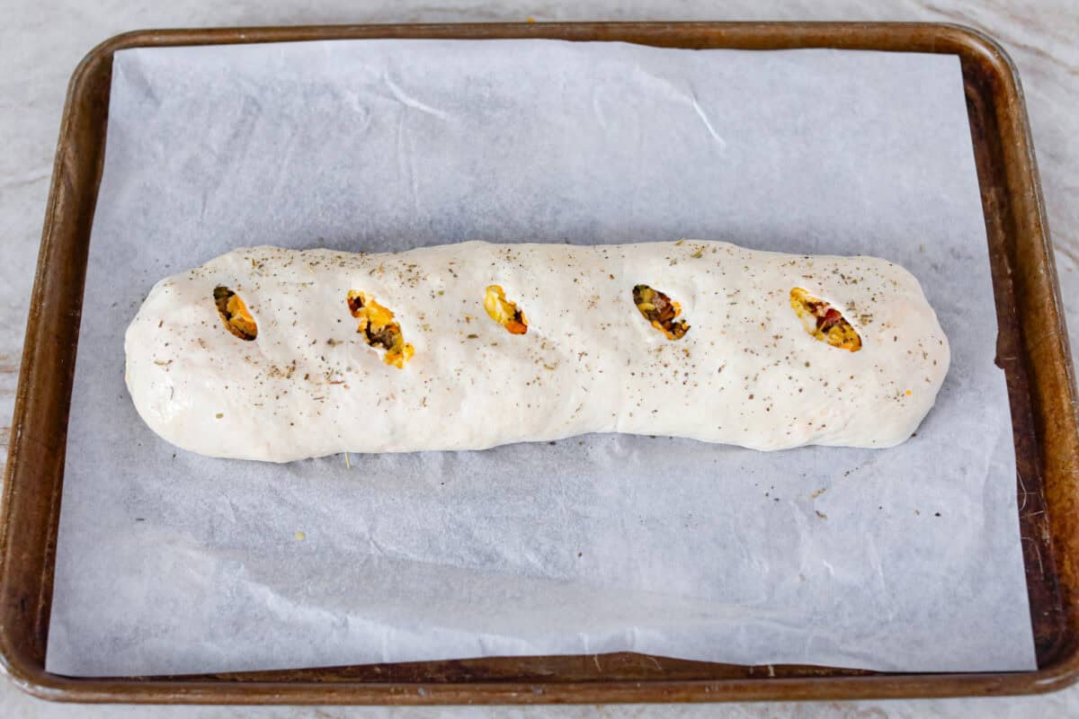 This Breakfast Stromboli is the best morning treat! It's packed with fluffy eggs, savory sausage, crispy bacon, and melty cheese, all wrapped in golden pizza dough. Perfect for holiday brunches or everyday family breakfasts! Overhead shot of the breakfast Stromboli with slits in the top and toped with italiand seasoning and garlic powder.
