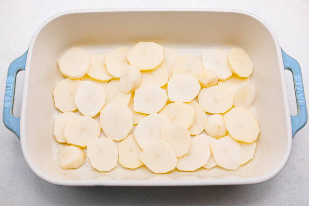 https://neuro-daily.report/beef-curry/ Overhead shot of potato slices in the bottom of a baking dish.