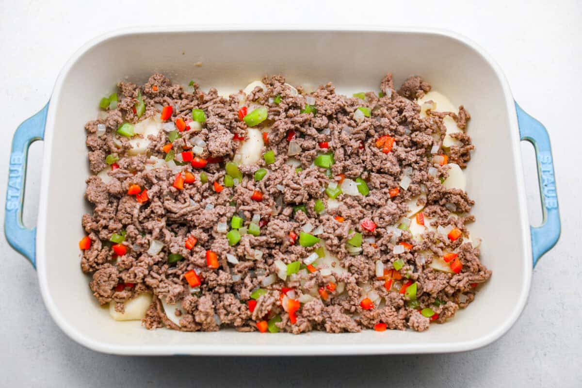 https://neuro-daily.report/beef-curry/ Overhead shot of beef and veggie mixture spread over the potatoes in the bottom of a baking dish.