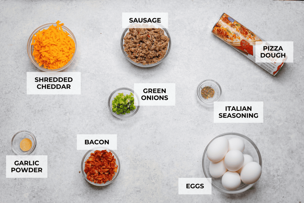 This Breakfast Stromboli is the best morning treat! It's packed with fluffy eggs, savory sausage, crispy bacon, and melty cheese, all wrapped in golden pizza dough. Perfect for holiday brunches or everyday family breakfasts! Overhead shot of labeled ingredients.
