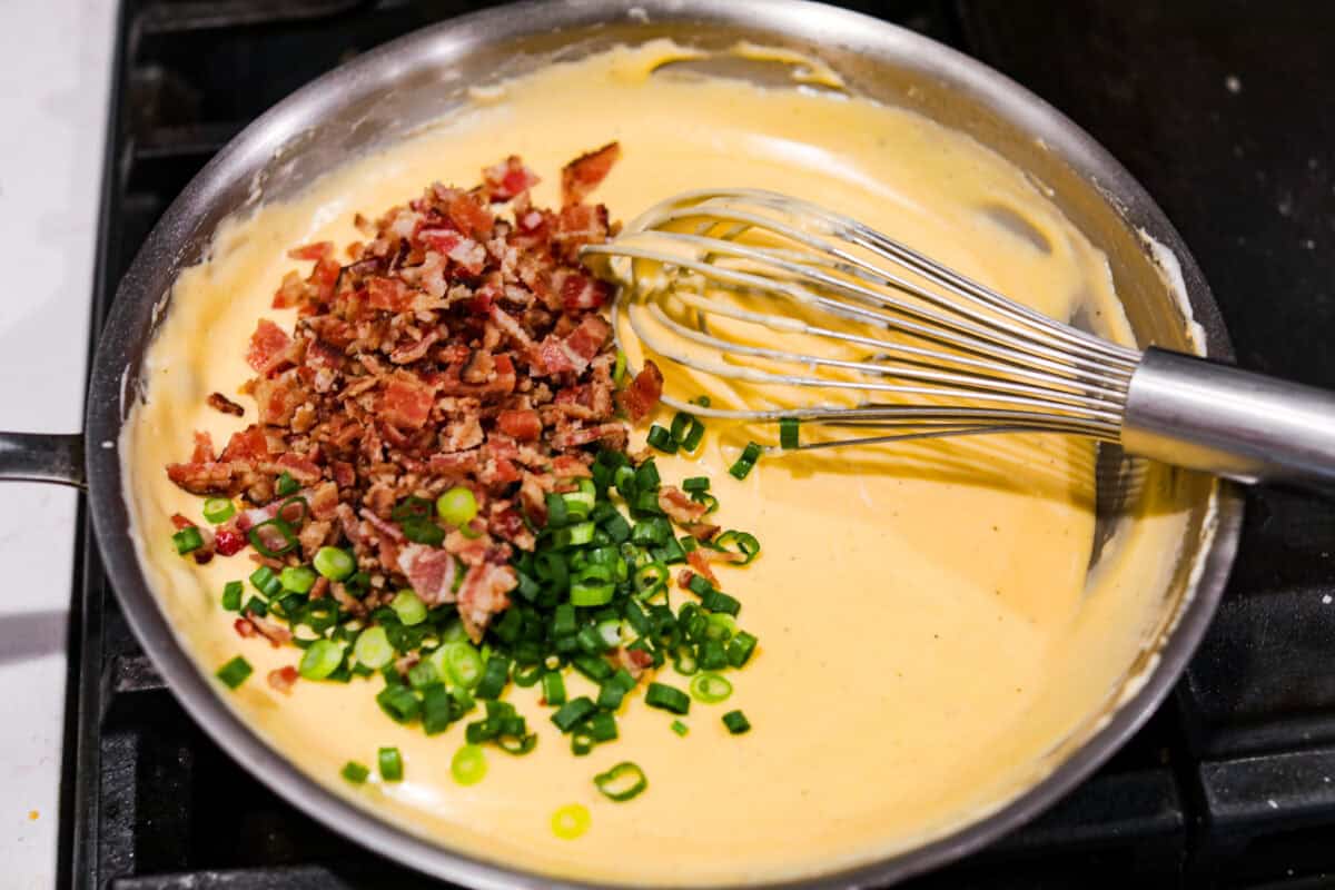 Loaded scalloped potatoes are rich, creamy, and "loaded" with flavor! This recipe combines tender potatoes baked to perfection in a velvety sauce topped with crispy bacon, green onions, and melty cheese. Overhead shot of someone whisking in the bacon and green onions into the sauce.
