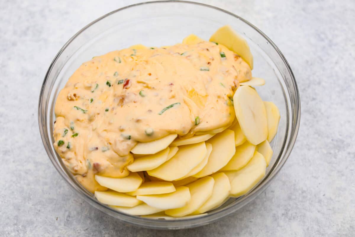 Loaded scalloped potatoes are rich, creamy, and "loaded" with flavor! This recipe combines tender potatoes baked to perfection in a velvety sauce topped with crispy bacon, green onions, and melty cheese. Overhead shot of the cheesy sauce poured over the sliced potatoes.