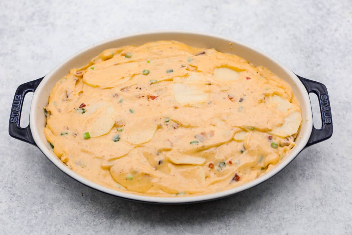 Loaded scalloped potatoes are rich, creamy, and "loaded" with flavor! This recipe combines tender potatoes baked to perfection in a velvety sauce topped with crispy bacon, green onions, and melty cheese. Overhead shot of the potatoes and sauce spread into a baking dish.