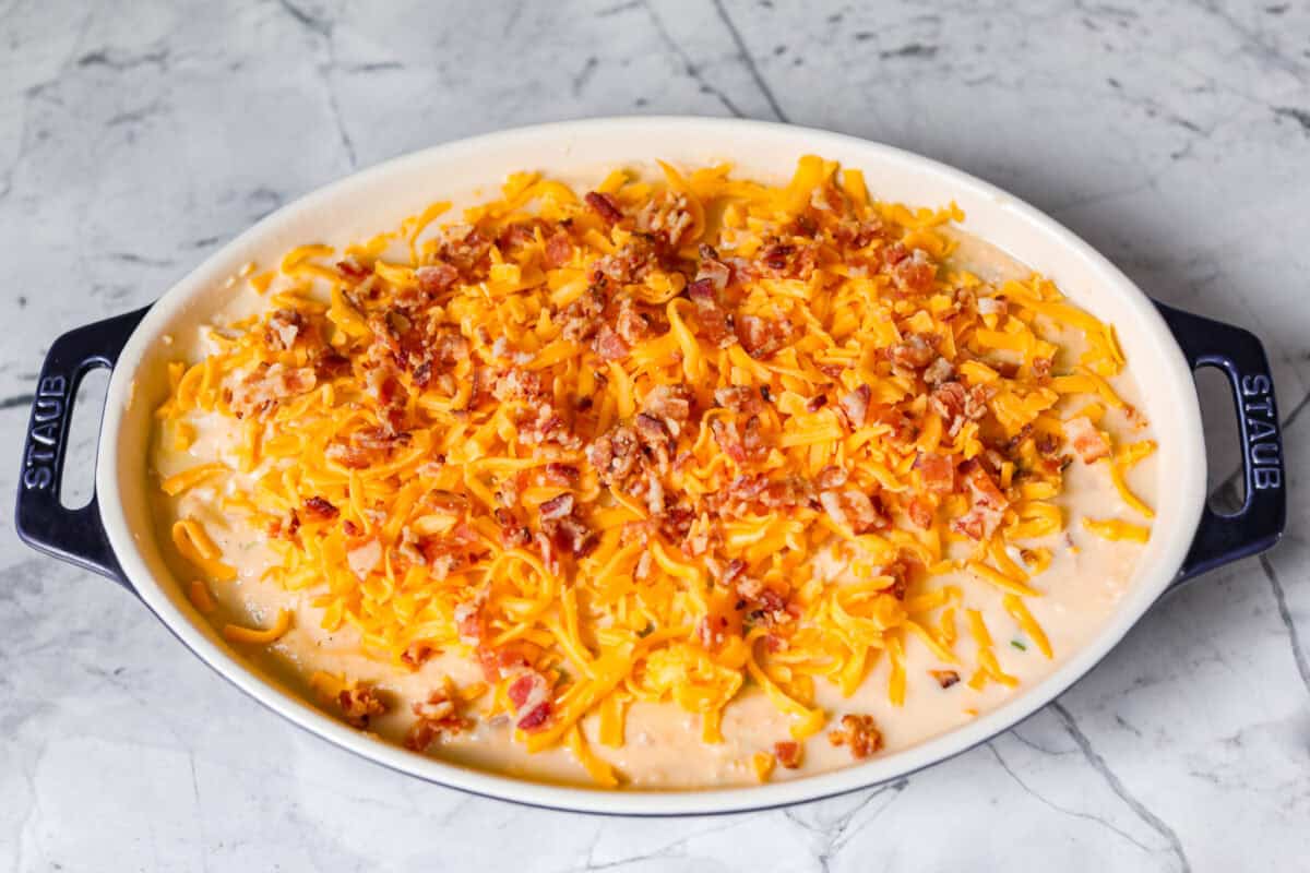 Loaded scalloped potatoes are rich, creamy, and "loaded" with flavor! This recipe combines tender potatoes baked to perfection in a velvety sauce topped with crispy bacon, green onions, and melty cheese. Overhead shot of cheese and bacon sprinkled over the top of the potatoes and sauce.