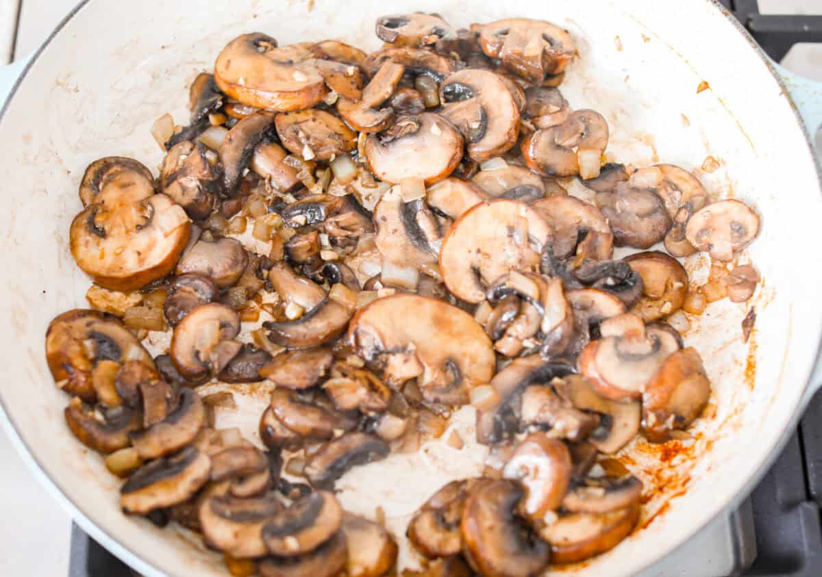Mushroom orzo is a tasty, comforting side dish! It combines tender orzo pasta with rich, earthy mushrooms in a creamy sauce. It’s easy to make and sure to impress with satisfying texture and savory flavors. overhead shot of mushrooms cooking in garlic in a skillet.