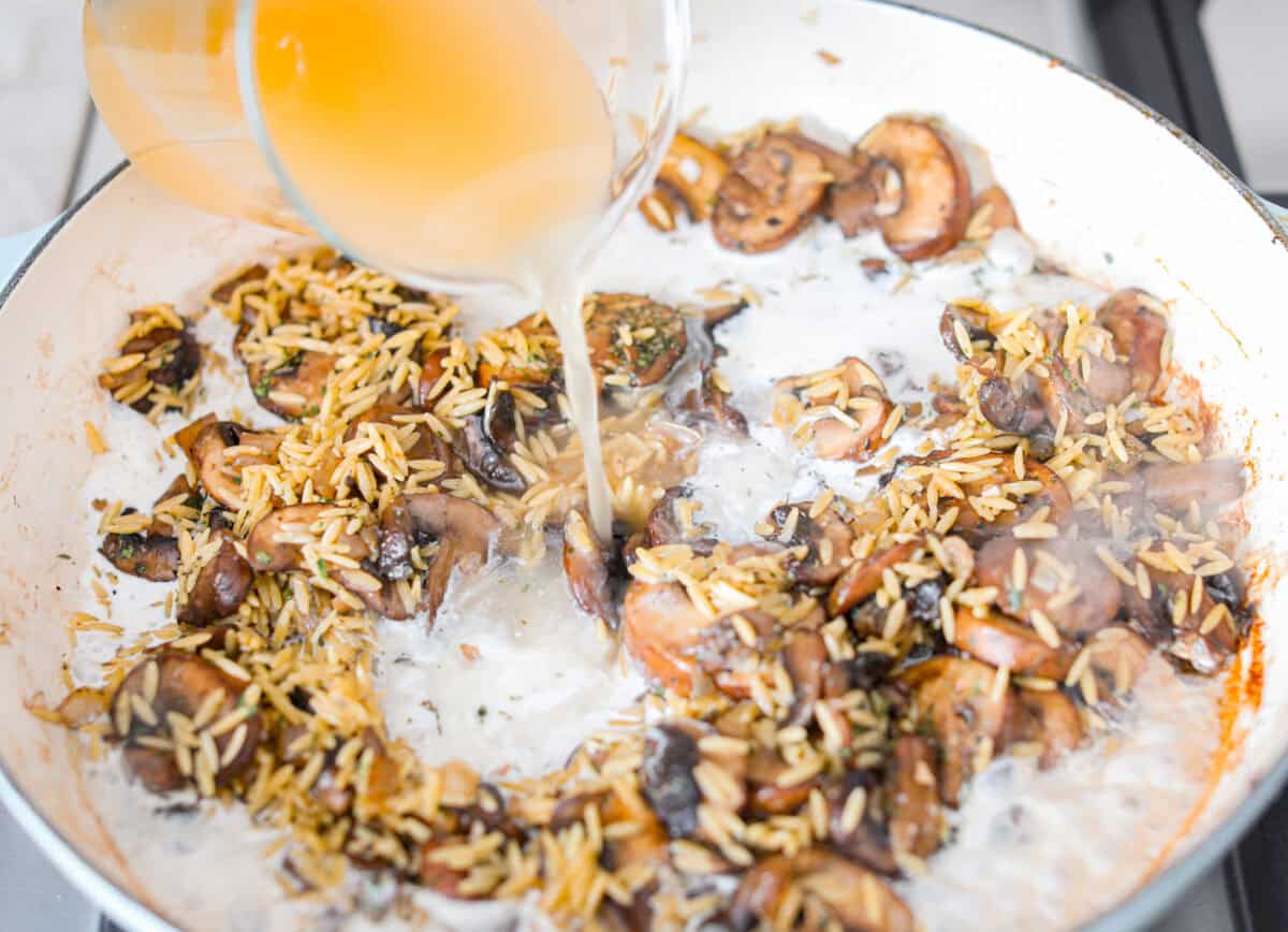 Mushroom orzo is a tasty, comforting side dish! It combines tender orzo pasta with rich, earthy mushrooms in a creamy sauce. It’s easy to make and sure to impress with satisfying texture and savory flavors. Angle shot of someone pouring cream and chicken broth in to the orzo and mushroom mixture.