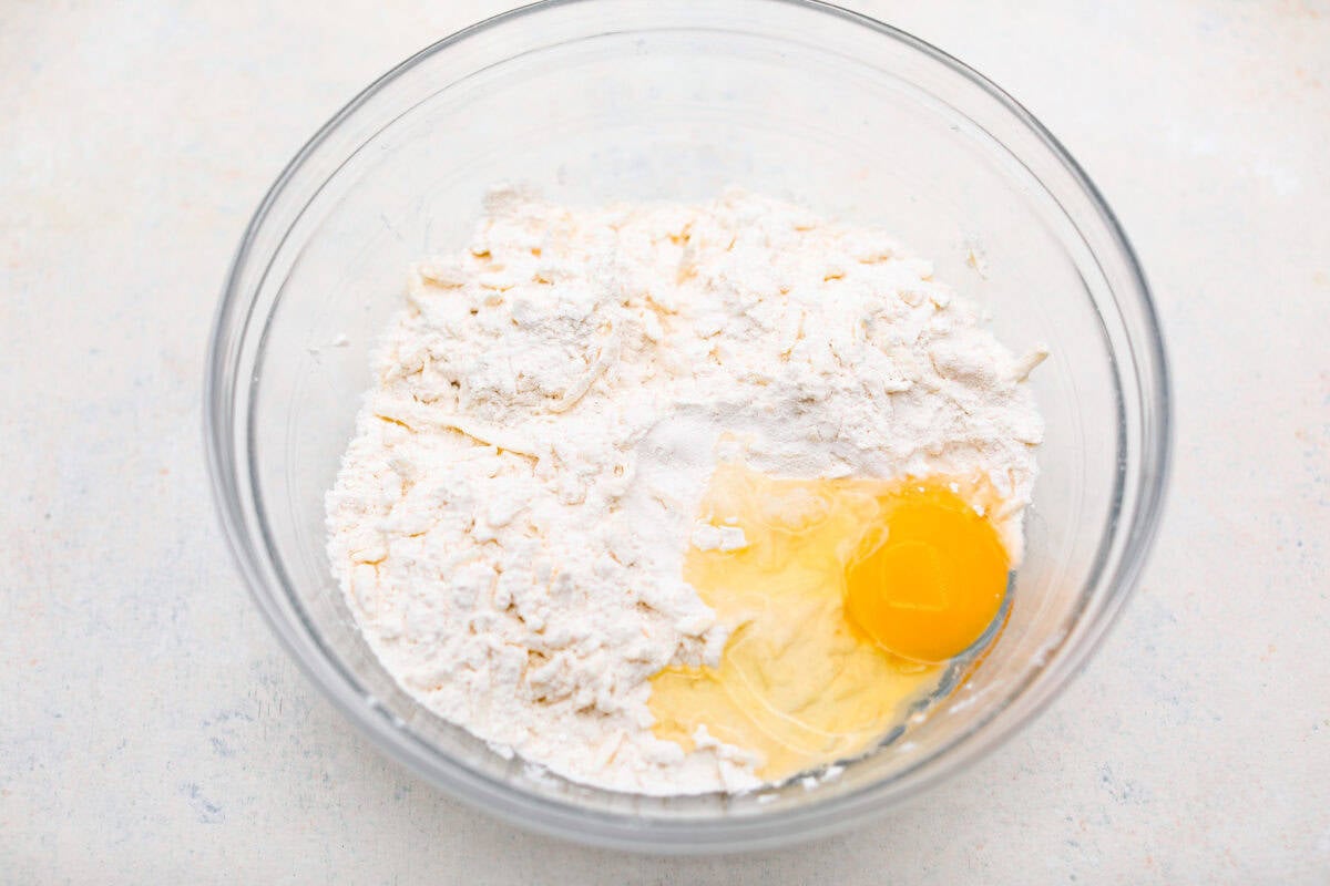 This creamy Ricotta Pie has a milky cinnamon flavor with a hint of lemon. The flavor is incredible, and it's surprisingly light for a cheese-based custard with its buttery shortbread crust. Overhead shot of the butter and dry ingredient mixture with an egg on top.