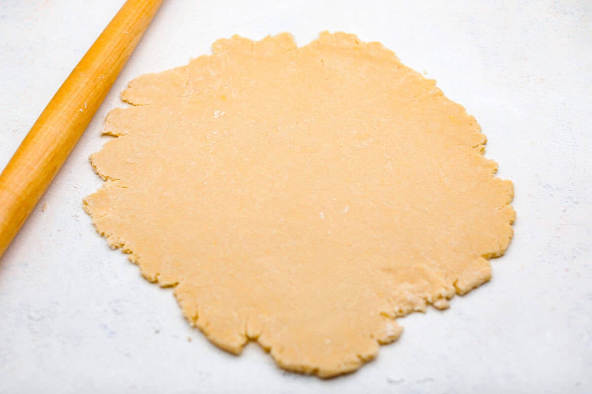 This creamy Ricotta Pie has a milky cinnamon flavor with a hint of lemon. The flavor is incredible, and it's surprisingly light for a cheese-based custard with its buttery shortbread crust. Overhead shot of the pie crust rolled out next to a rolling pin.