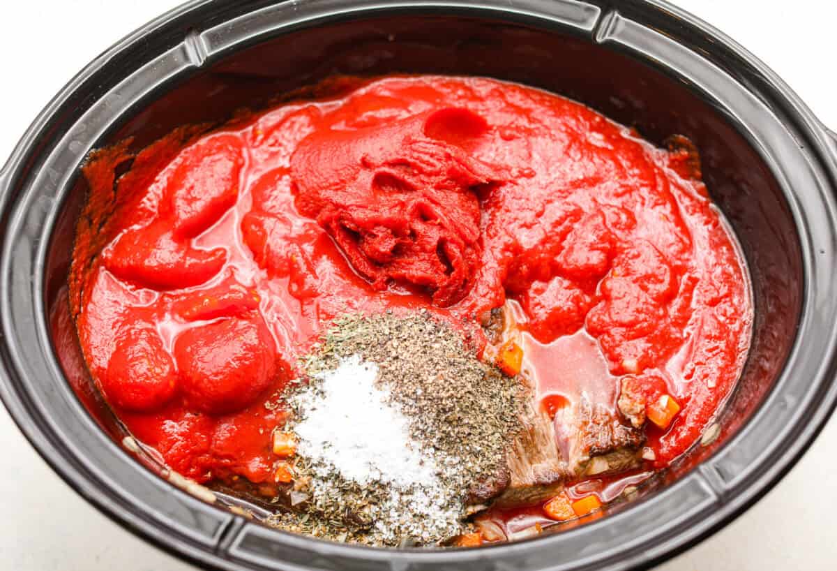 Slow cooker Sunday sauce, also known as "sugo," is a rich, tomato-based ragu that’s a favorite for family dinners. Traditionally, it's simmered low and slow from morning until dinnertime, making it a perfect recipe for the Crockpot. Serve it over pasta with a sprinkle of pecorino romano cheese for an unforgettable meal! Overhead shot of all of the ingredients added to the slow cooker.