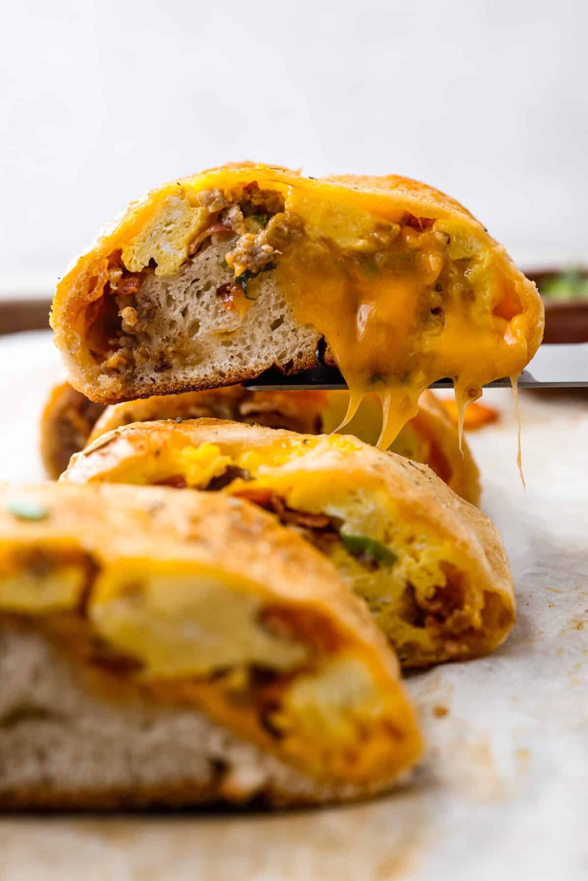 This Breakfast Stromboli is the best morning treat! It's packed with fluffy eggs, savory sausage, crispy bacon, and melty cheese, all wrapped in golden pizza dough. Perfect for holiday brunches or everyday family breakfasts! Side shot of breakfast Stromboli cut and a piece being lifted up with a spatula.