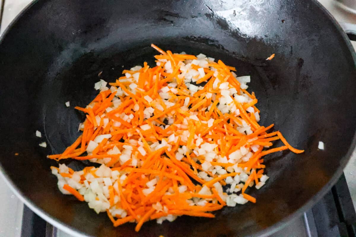 Delicious crab fried rice comes together in just 25 minutes with simple ingredients and tons of flavor! It combines the sweetness of lump crab meat with the savory flavors of classic fried rice for an endlessly satisfying dish that's sure to become a family favorite! Overhead shot of carrots, onions and sesame oil cooking in a skillet.