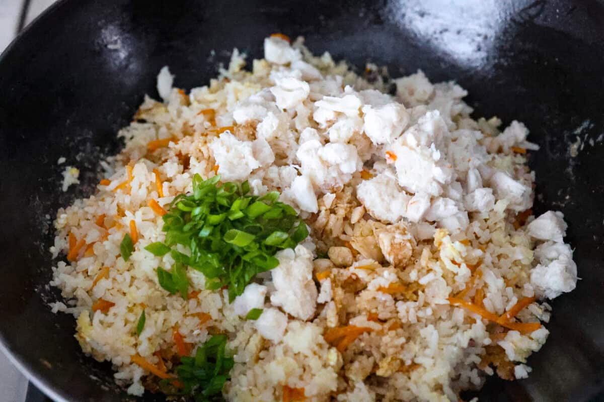 Delicious crab fried rice comes together in just 25 minutes with simple ingredients and tons of flavor! It combines the sweetness of lump crab meat with the savory flavors of classic fried rice for an endlessly satisfying dish that's sure to become a family favorite! Angle shot of the crab, green onions, soy sauce and lime juice on top of the rice, veggie and egg mixture.