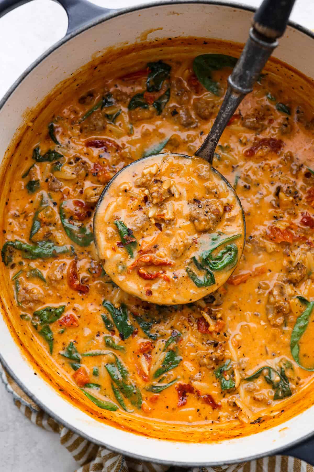 Warm up to this delicious Marry Me sausage orzo soup! It's hearty, super flavorful, and packed with seasoned sausage, tender orzo pasta, and plenty of bold, savory seasonings. Overhead shot of marry me sausage orzo soup in a pot with a ladle.