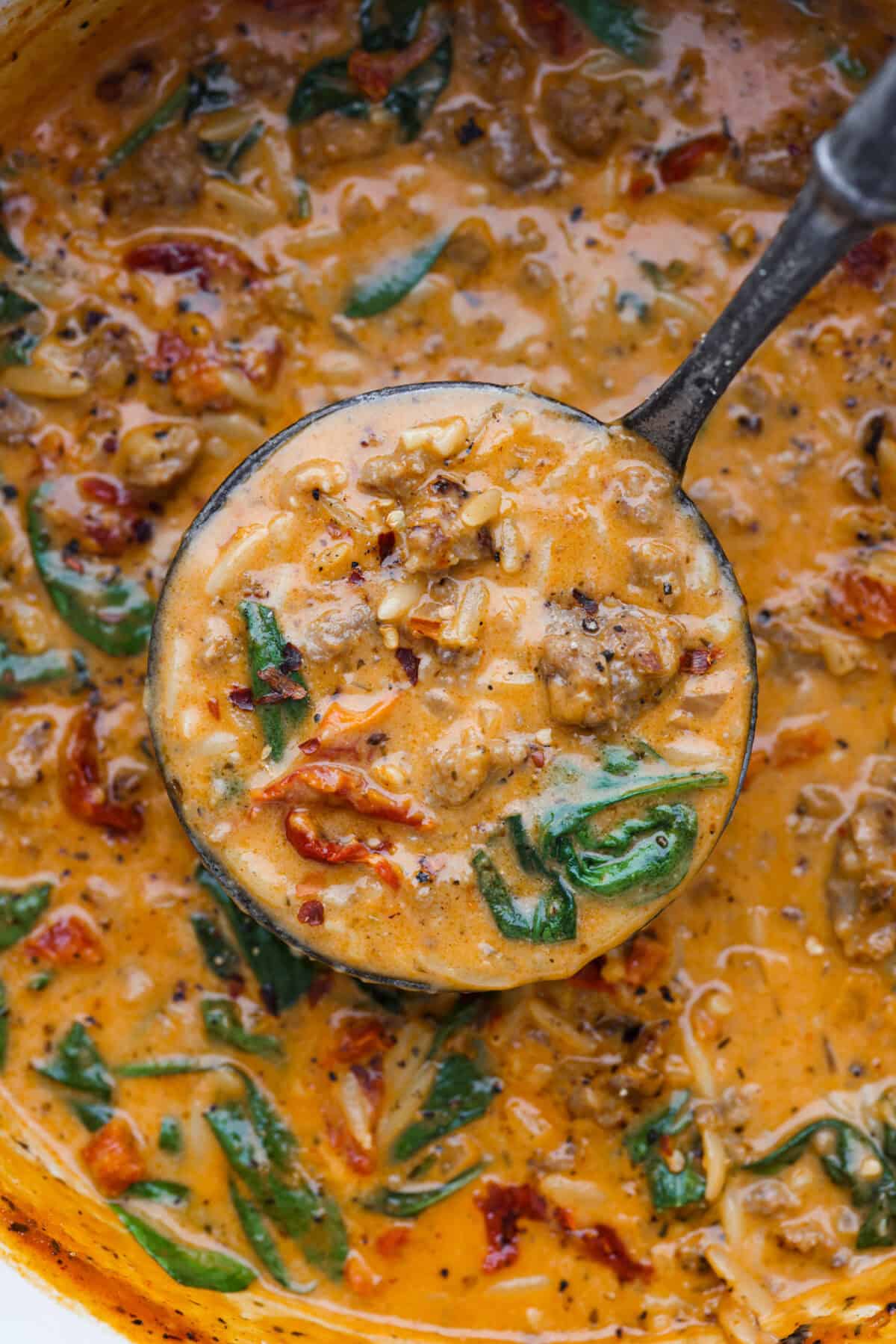 Warm up to this delicious Marry Me sausage orzo soup! It's hearty, super flavorful, and packed with seasoned sausage, tender orzo pasta, and plenty of bold, savory seasonings. Close up shot of marry me sausage orzo soup in a ladle over the pot of soup.