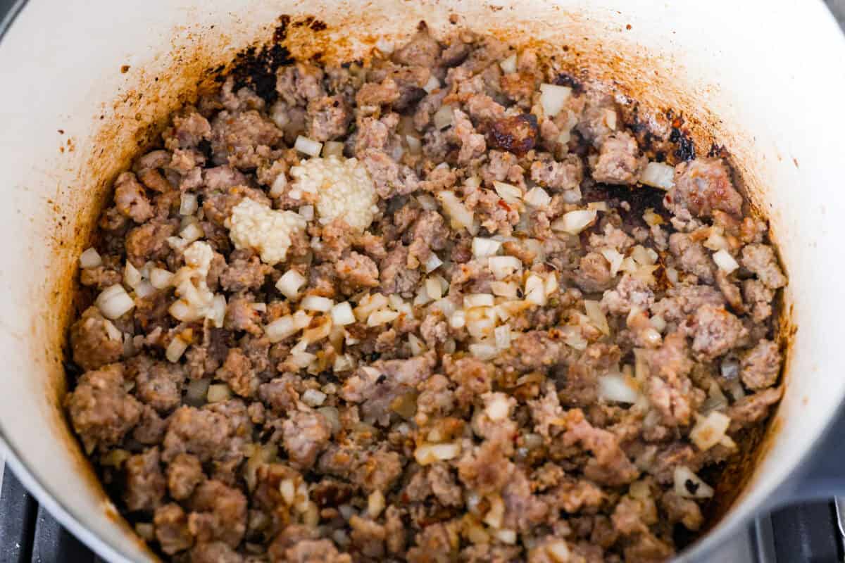 Warm up to this delicious Marry Me sausage orzo soup! It's hearty, super flavorful, and packed with seasoned sausage, tender orzo pasta, and plenty of bold, savory seasonings. Overhead shot of sausage and onions cooking in a pot.