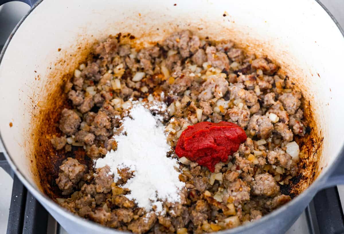 Warm up to this delicious Marry Me sausage orzo soup! It's hearty, super flavorful, and packed with seasoned sausage, tender orzo pasta, and plenty of bold, savory seasonings. Overhead shot of sausage and onions with flour and tomato paste added to it.