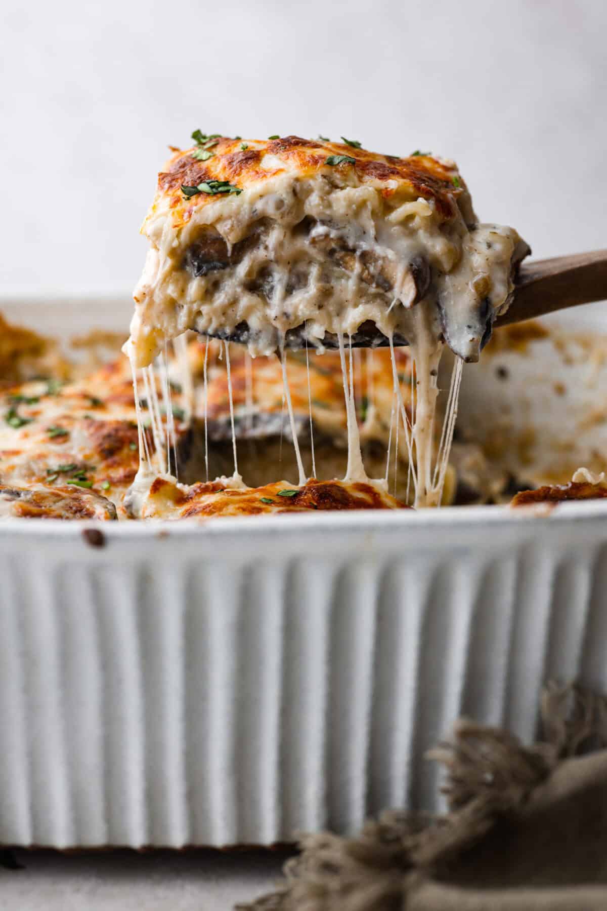 This creamy, cheesy mushroom lasagna is a delicious twist on the classic. Instead of traditional meat and red sauce, this recipe features layers of garlicky mushrooms and a rich bechamel sauce that brings incredible depth to every bite. Side shot of a piece of mushroom lasagna being lifted out of the baking dish with a wooden spatula.