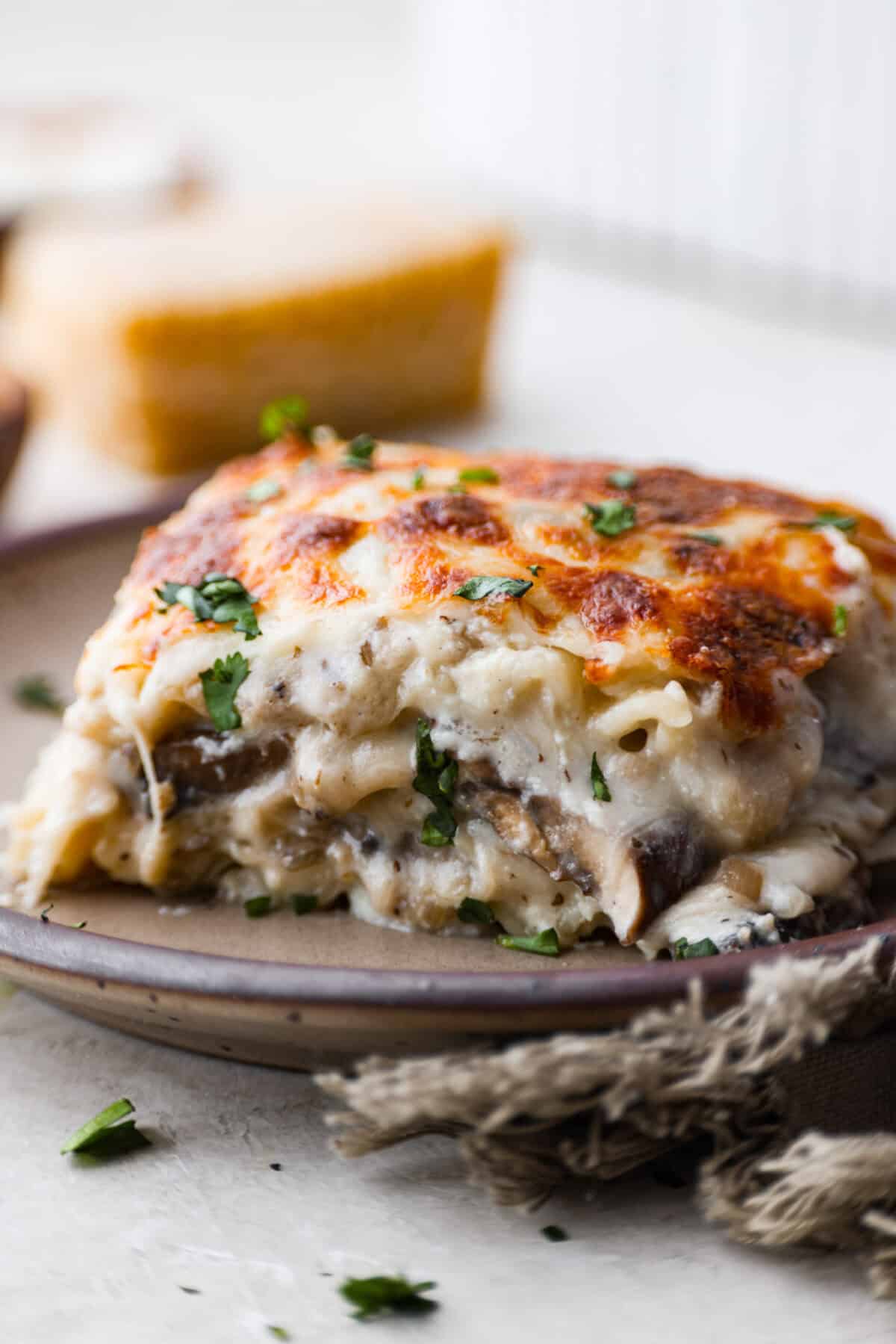 This creamy, cheesy mushroom lasagna is a delicious twist on the classic. Instead of traditional meat and red sauce, this recipe features layers of garlicky mushrooms and a rich bechamel sauce that brings incredible depth to every bite. Side shot of a plated slice of mushroom lasagna.