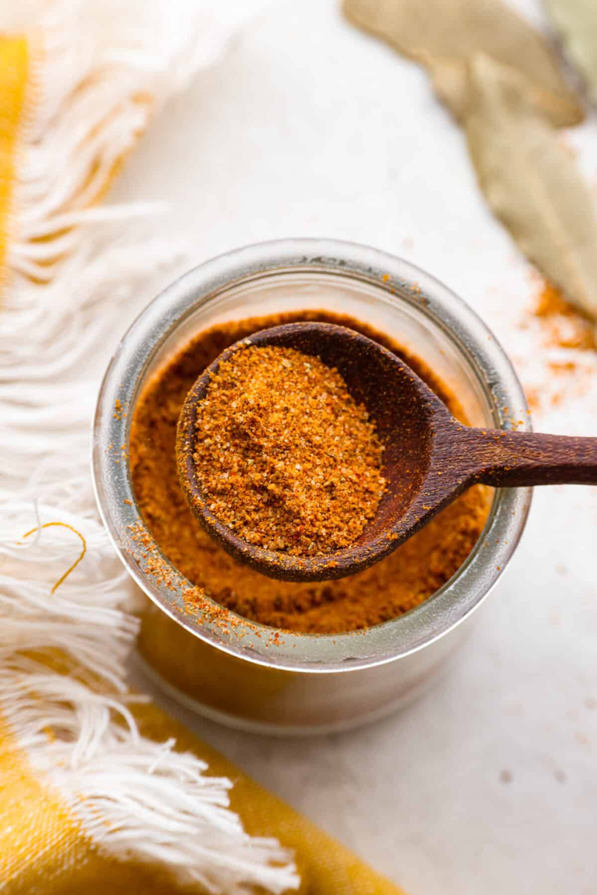 Homemade Old Bay Seasoning is a simple way to bring bold, zesty flavor to your dishes! This spice blend has a classic taste but with the freshness and flexibility of making it yourself. Perfect for seafood, meats, and more! Overhead shot of someone lifting a scoop of seasoning from a jar of homemade old bay seasoning.