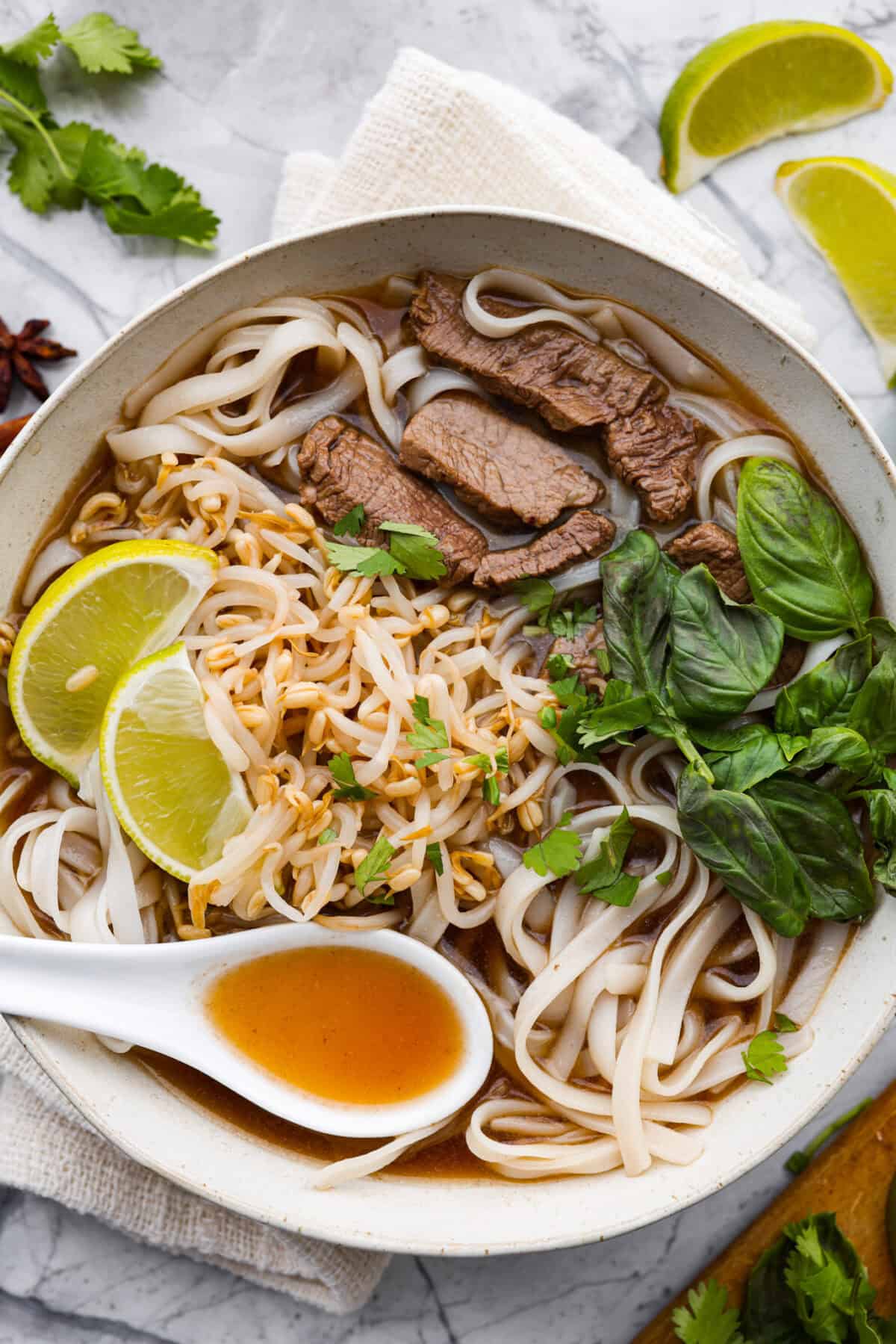 This simplified version of Vietnamese noodle soup brings the comforting flavors you love in Pho but with less effort. For a truly authentic experience, donโt miss out on this detailed recipe! Overhead shot of Vietnamese noodle soup garnished with lime wedges, cilantro and Thai basil.