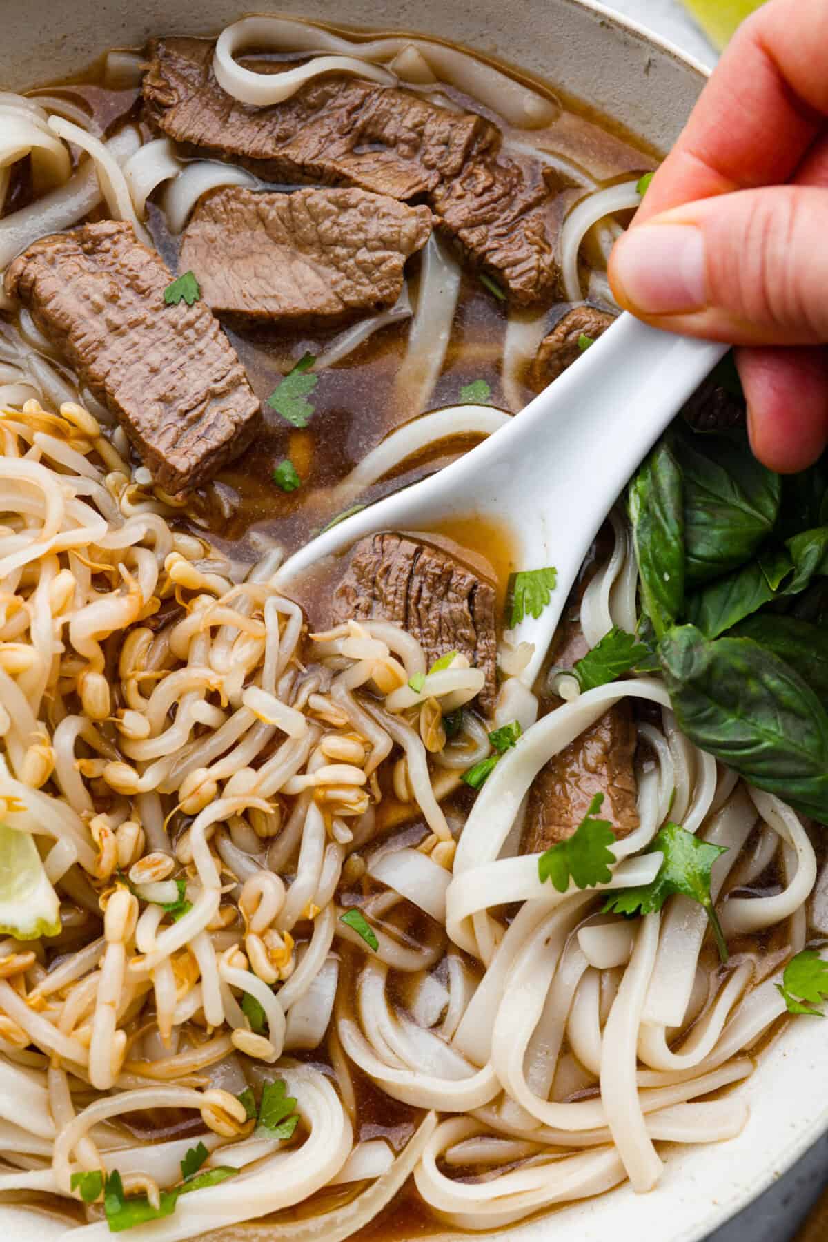 This simplified version of Vietnamese noodle soup brings the comforting flavors you love in Pho but with less effort. For a truly authentic experience, donโt miss out on this detailed recipe! Close up shot of someone getting a spoonful of Vietnamese noodle soup from the bowl.