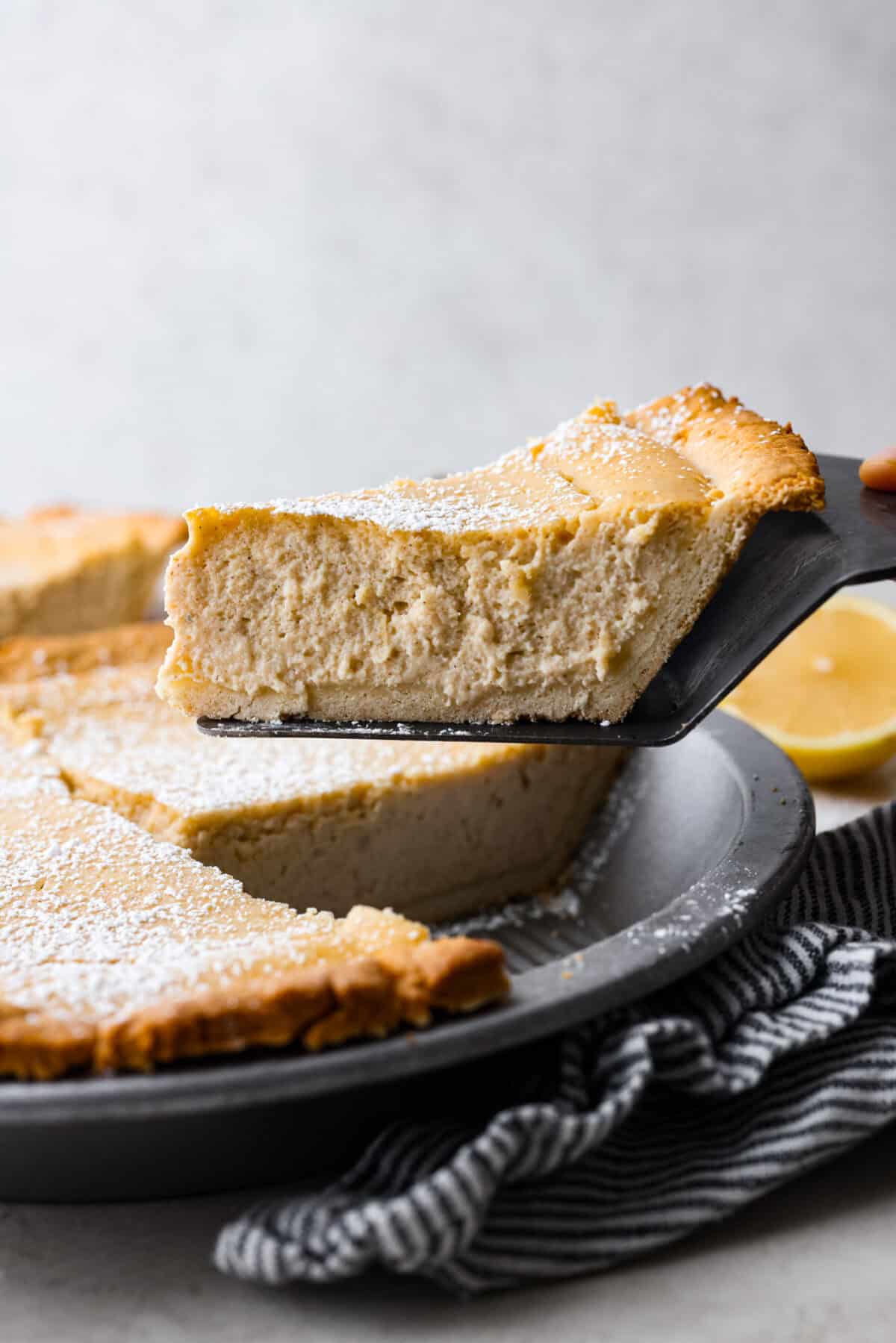 This creamy Ricotta Pie has a milky cinnamon flavor with a hint of lemon. The flavor is incredible, and it's surprisingly light for a cheese-based custard with its buttery shortbread crust. Side shot of a slice of ricotta pie being lifted out of the whole pie pan.