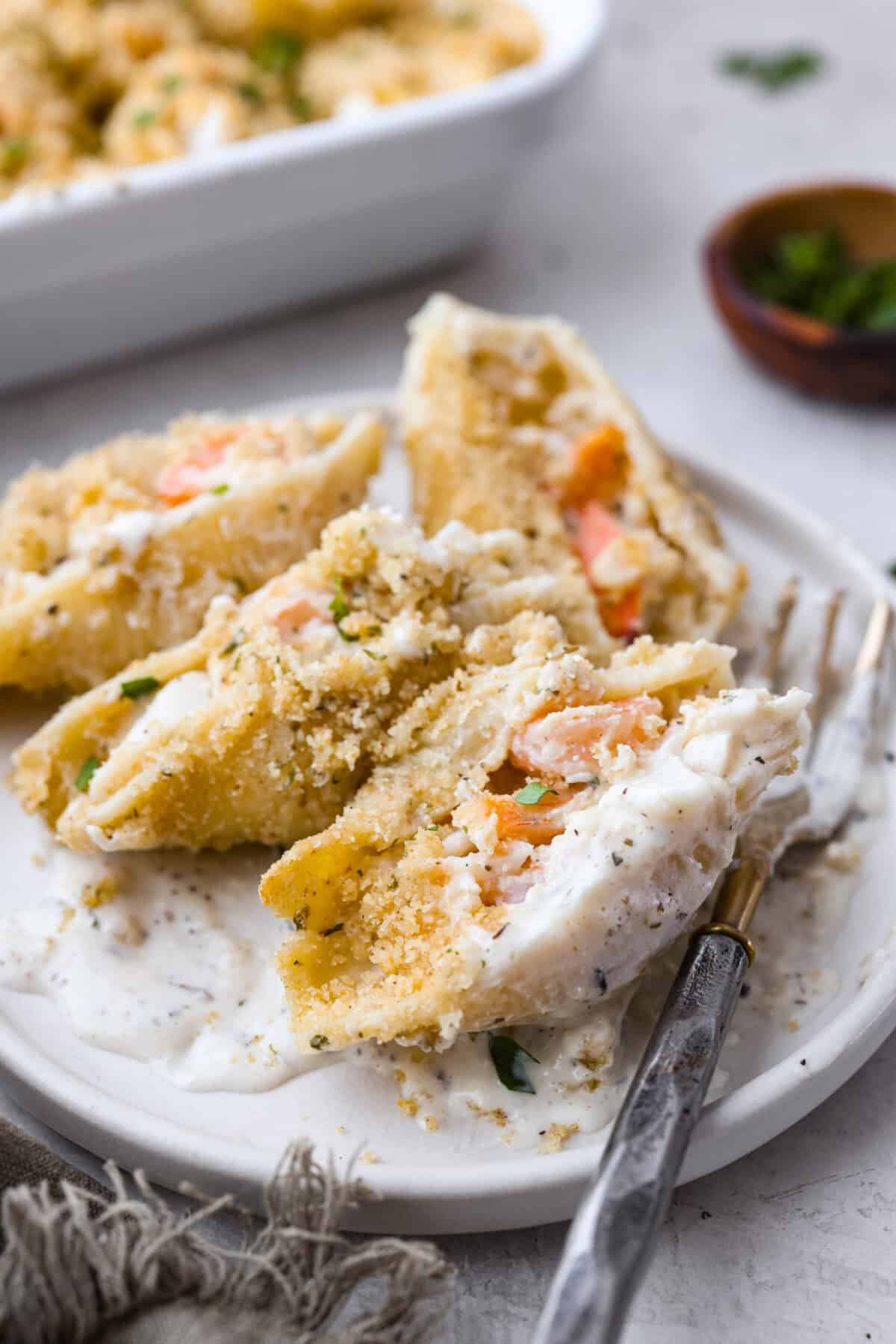 Seafood Stuffed Shells is a comforting meal that's sure to impress! Jumbo pasta shells are generously filled with a creamy, savory seafood filling and coated in a rich Alfredo-based sauce. Finish with a crispy crumb topping for an irresistible dinner! Side shot of plated seafood stuffed shells.