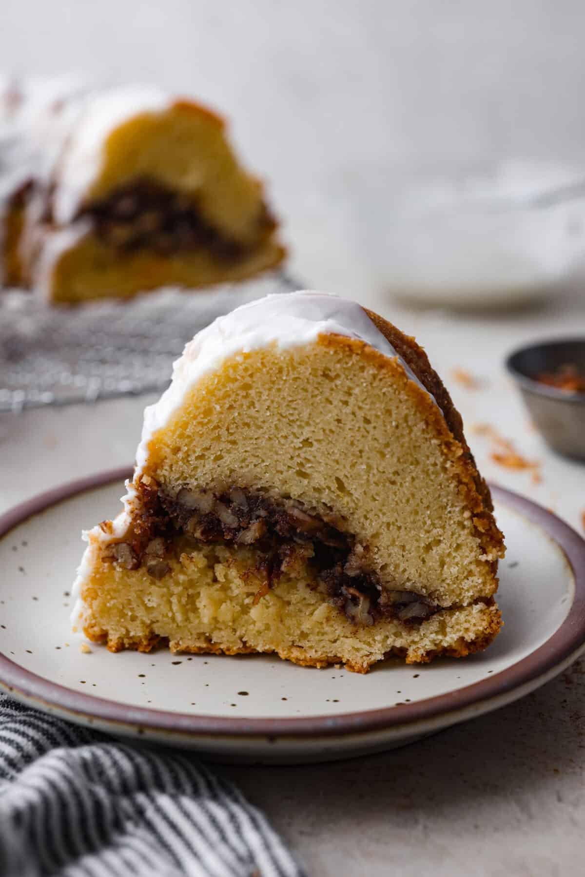 This Sock It to Me Cake is a moist, buttery Southern bundt cake with a delicious cinnamon-sugar pecan layer swirled through the middle. It became popular because of Duncan Hines in the 1960s and 1970s, and you'll understand why once you try it! Side shot of a slice of sock it to me cake on a plate.