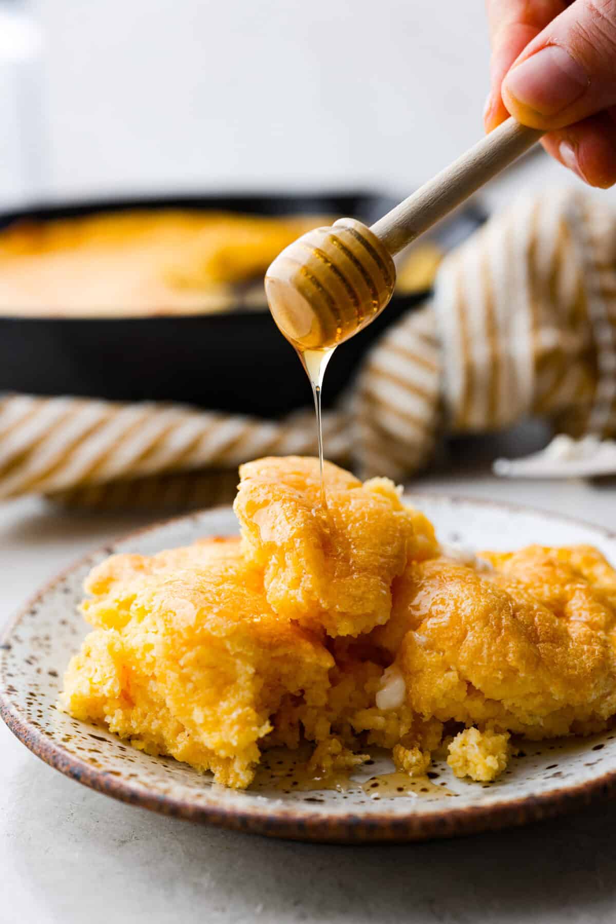 Spoon bread is a beloved classic Southern side dish. It’s similar to cornbread but is less sweet and has a softer, almost soufflé-like texture. This unique bread is best enjoyed warm with a dollop of butter, a drizzle of honey or served alongside a hearty bowl of chili. Side shot of a plated piece of spoon bread with honey being drizzled over the top.
