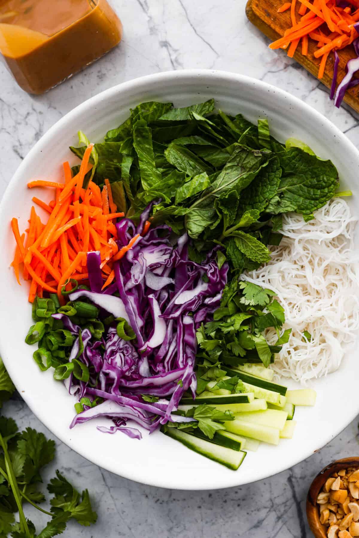 This flavorful, fresh Spring Roll Bowl is not only insanely delicious but absolutely beautiful. It's filled with tender rice vermicelli, vibrant vegetables, and fresh herbs, all topped with my Thai peanut dressing. Close up shot of all of the ingredients added to a spring roll bowl, but they haven't been mixed together.