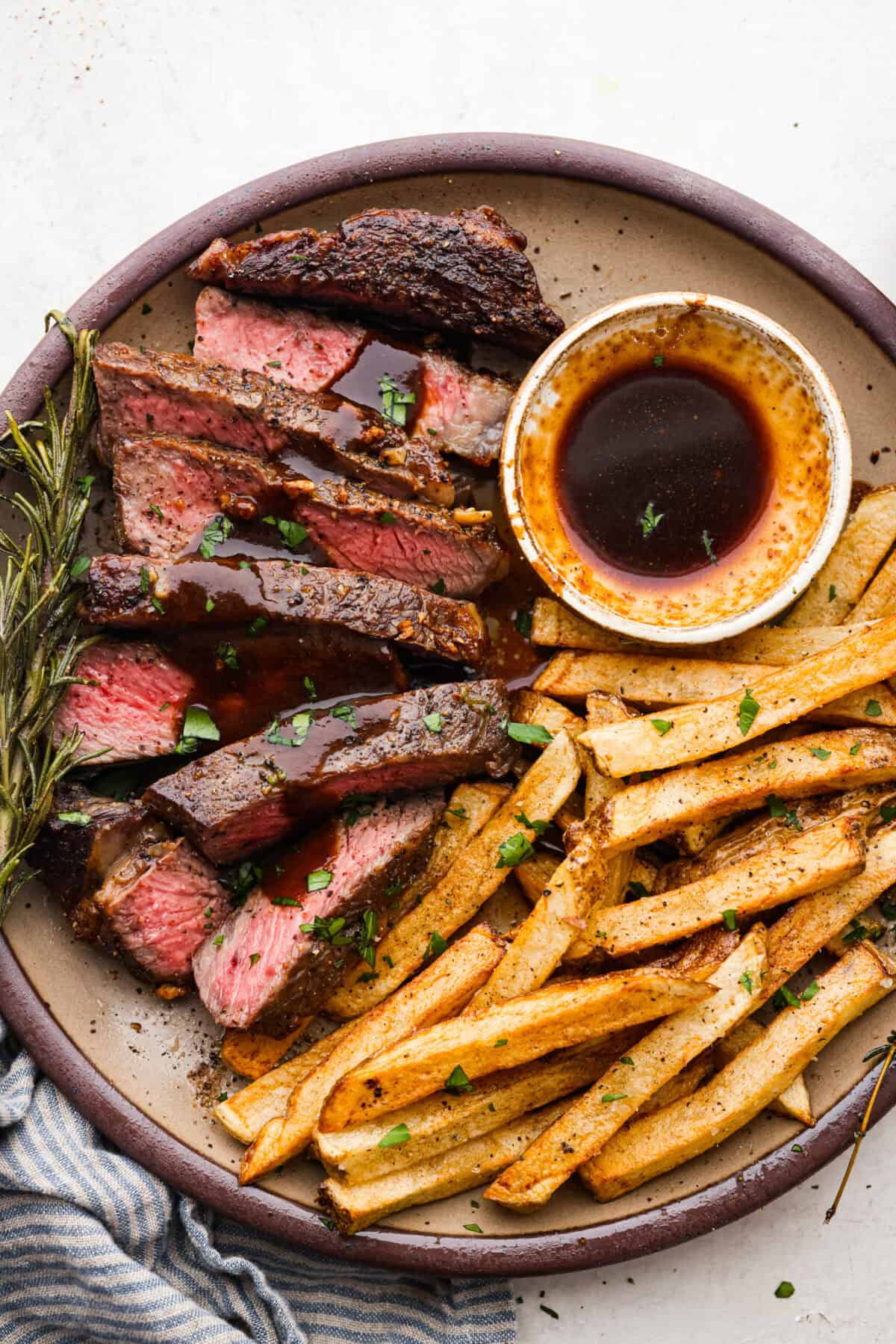 Steak Frites is a classic French bistro dish that combines perfectly seared, juicy steak with crispy, golden fries. It's a simple yet delicious meal that is filled with rich flavors and satisfying crunch. You will love this restaurant-quality dinner made right in your own kitchen! Overhead shot of plated and sliced steak frites.