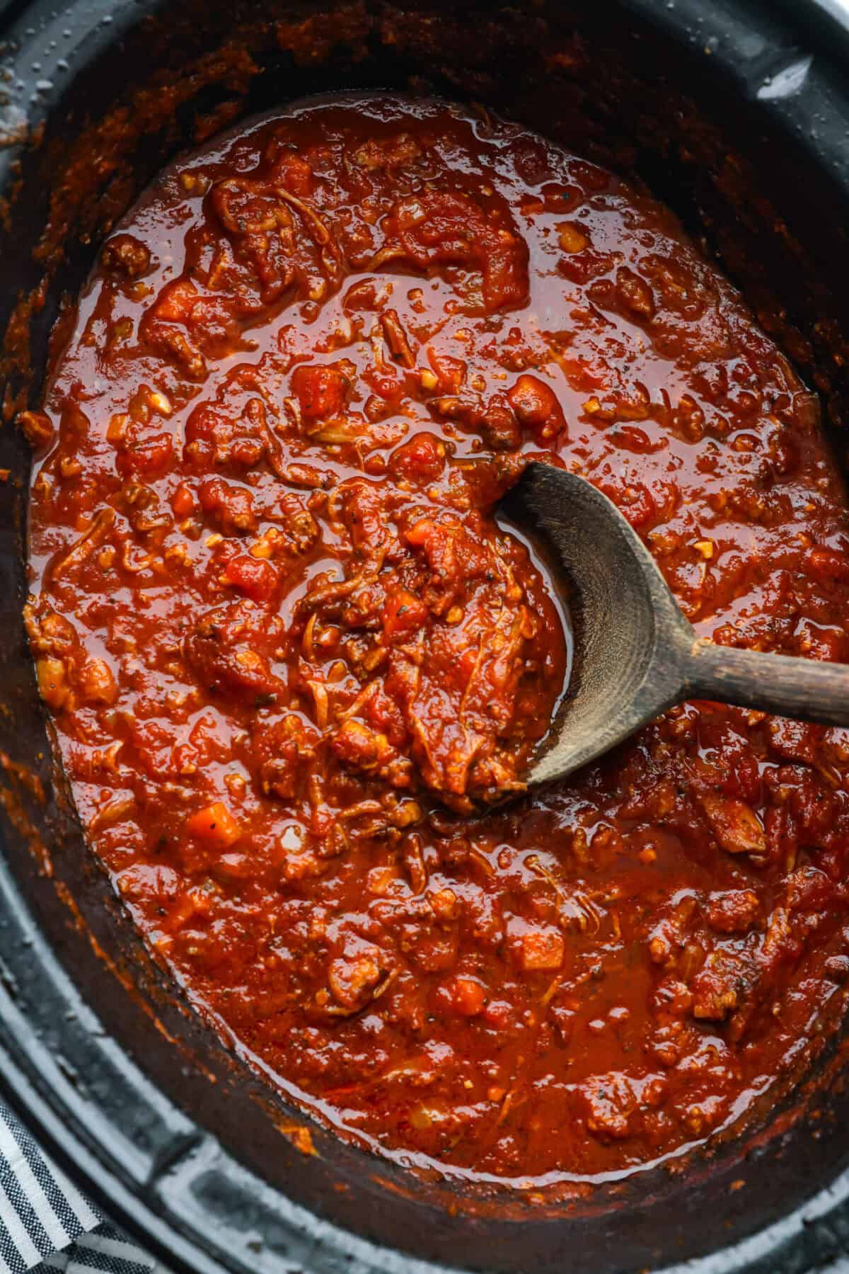 Slow cooker Sunday sauce, also known as "sugo," is a rich, tomato-based ragu that’s a favorite for family dinners. Traditionally, it's simmered low and slow from morning until dinnertime, making it a perfect recipe for the Crockpot. Serve it over pasta with a sprinkle of pecorino romano cheese for an unforgettable meal! Overhead shot of slow cooker Sunday sauce in a crockpot.