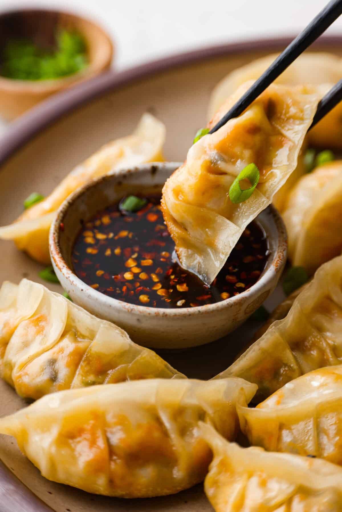These vegetable dumplings are so full of Asian flavor, you won’t be able to stop at just one! Tender wontons are filled with an incredible veggie mixture that's infused with ginger, soy sauce, sesame oil and garlic. Like a potsticker without the meat! Close up whot of someone using chopsticks to dip a vegetable dumpling into some sauce.
