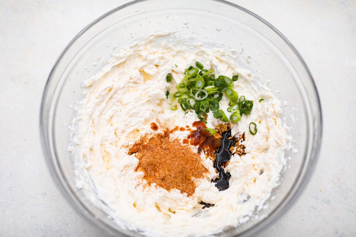 Spice up your appetizer game with Cajun Crab Dip! Packed with tender crab meat, bold Cajun seasoning, and a luscious, creamy base. This dip is irresistibly rich and full of flavor. Serve this at your next gathering with your favorite crispy crackers! Overhead shot of green onion, lemon juice, seasonings, hot sauce and Worcestershire sauce on top of the cream cheese mixture.