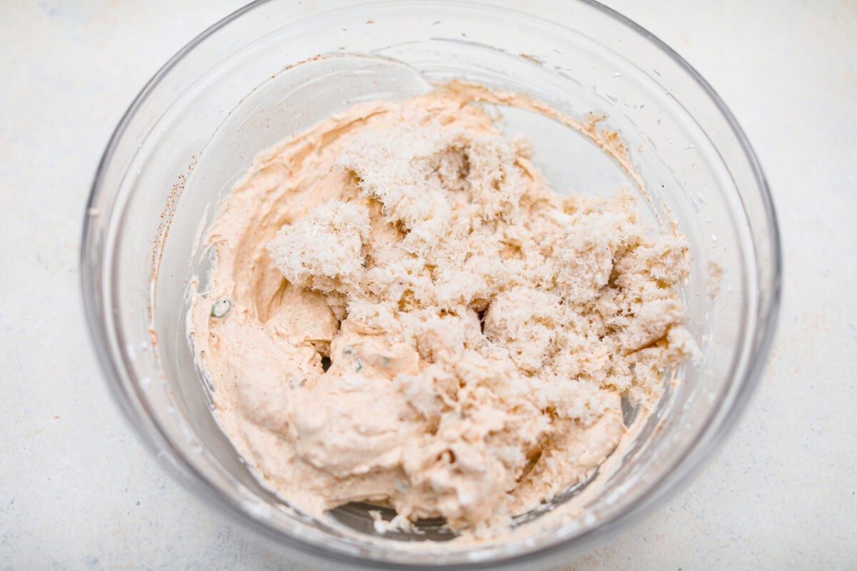 Spice up your appetizer game with Cajun Crab Dip! Packed with tender crab meat, bold Cajun seasoning, and a luscious, creamy base. This dip is irresistibly rich and full of flavor. Serve this at your next gathering with your favorite crispy crackers! Overhead shot of crab meat added to the cream cheese and seasoning mixture in a mixing bowl.