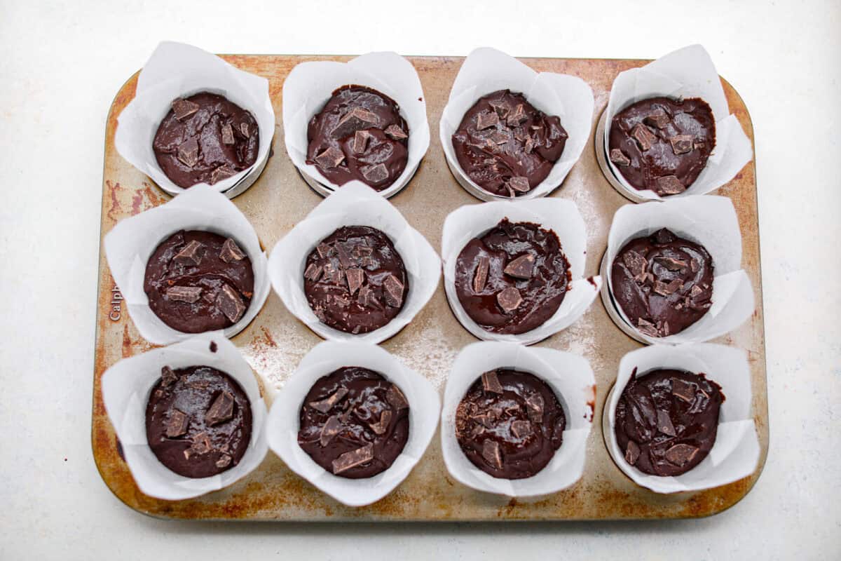 These double chocolate muffins are rich, moist, and packed with deep chocolate flavor! They are the perfect treat for breakfast, snack time, or dessert. They come together with simple ingredients and bake up beautifully with a soft, tender crumb in less than an hour! Overhead shot of the chocolate muffin batter in each muffin liner in the muffin tin.