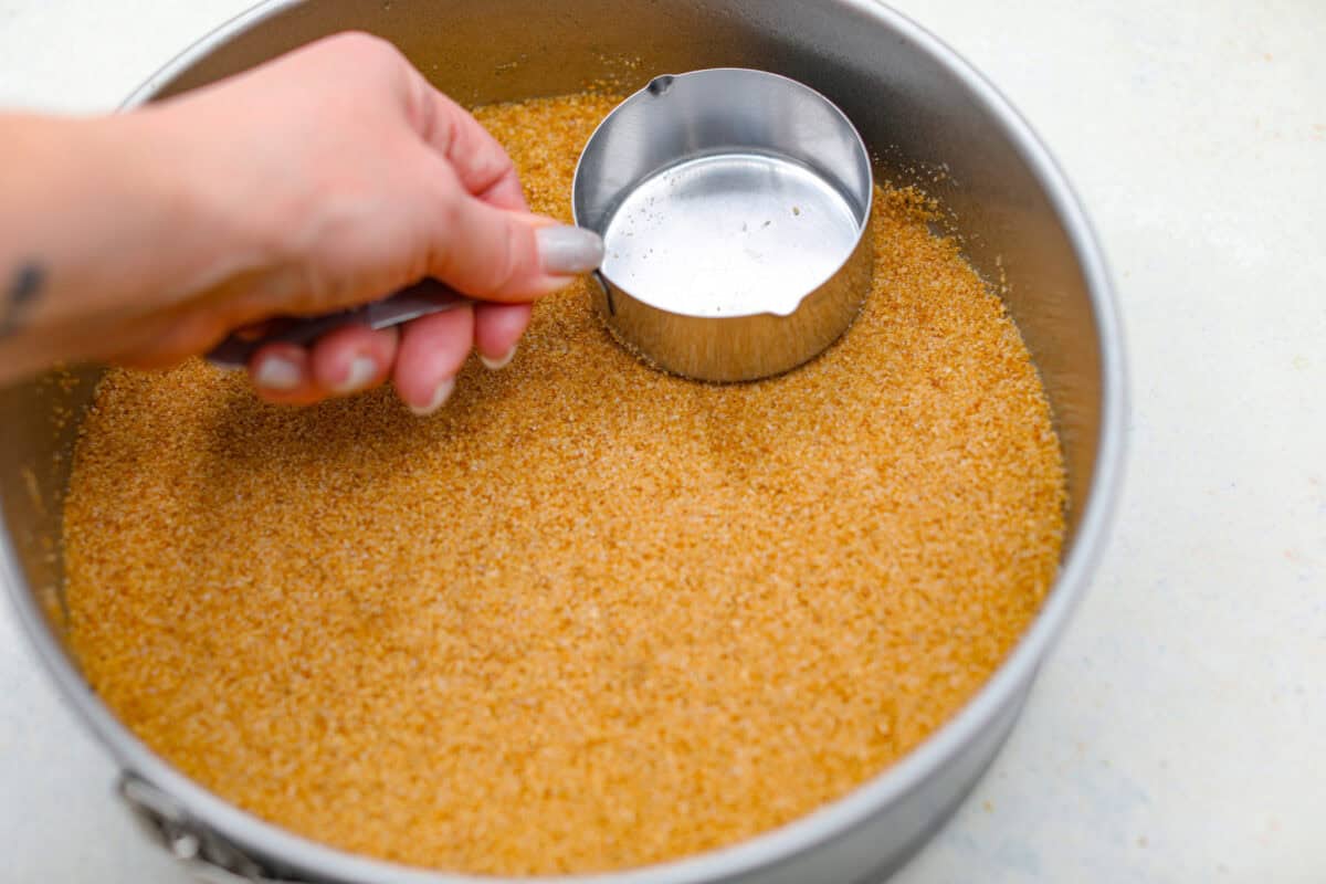 Creme Brulee Cheesecake is the perfect merging of two beloved desserts! It has the rich, creamy texture of cheesecake with the caramelized sugar topping of classic crรจme brรปlรฉe. This irresistible treat is the best of both worlds! Pressing graham cracker crumbs into a springform pan.
