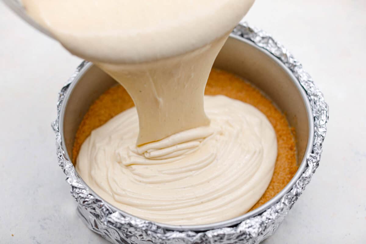 Creme Brulee Cheesecake is the perfect merging of two beloved desserts! It has the rich, creamy texture of cheesecake with the caramelized sugar topping of classic crรจme brรปlรฉe. This irresistible treat is the best of both worlds! Pouring cheesecake mixture into a pan.
